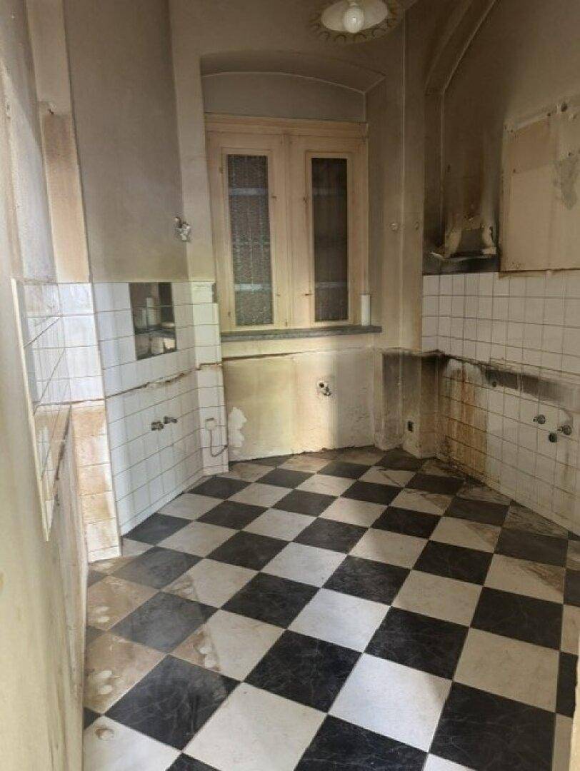 Küche in einem Altbau mit charakteristischem schwarz-weiß kariertem Fliesenboden und Fenster.