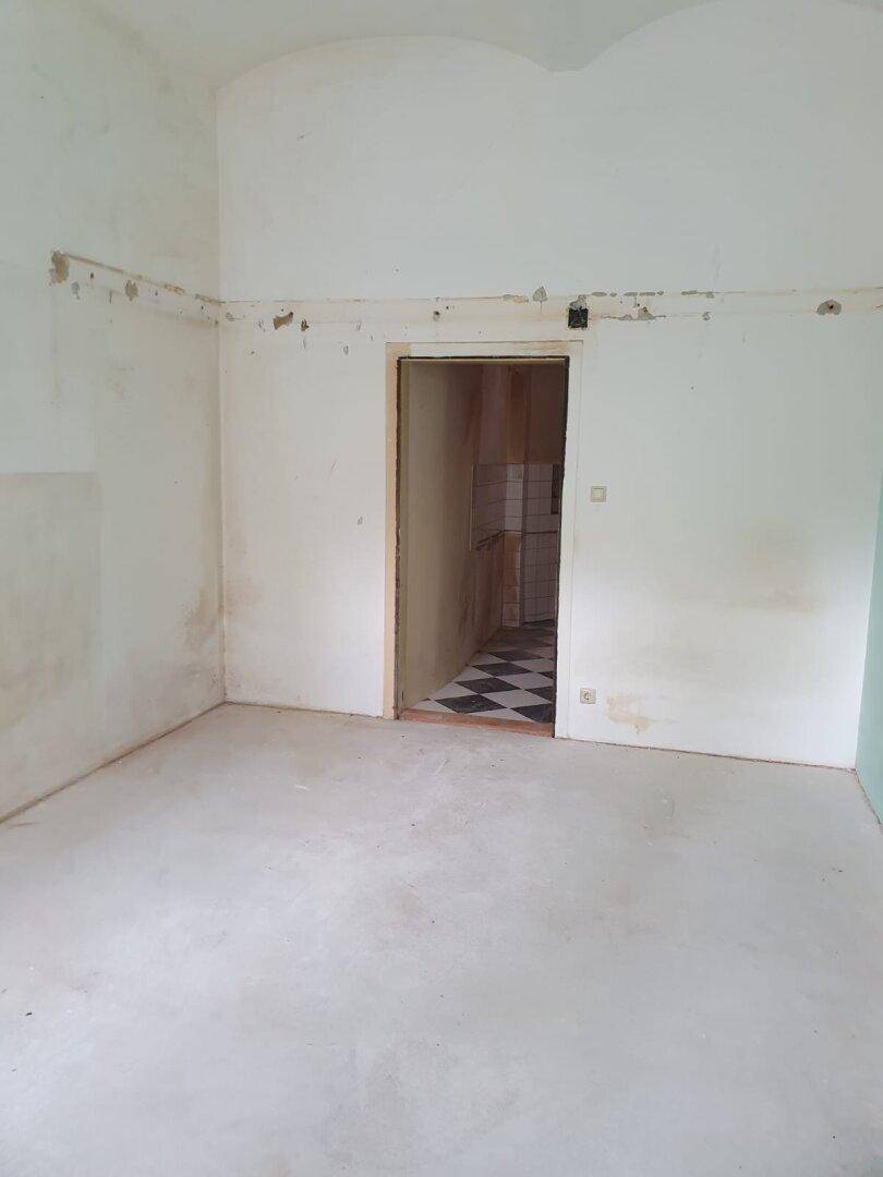 Unfertiger Raum mit Zugang zu einem weiteren Zimmer mit Schachbrettmuster-Musterboden.