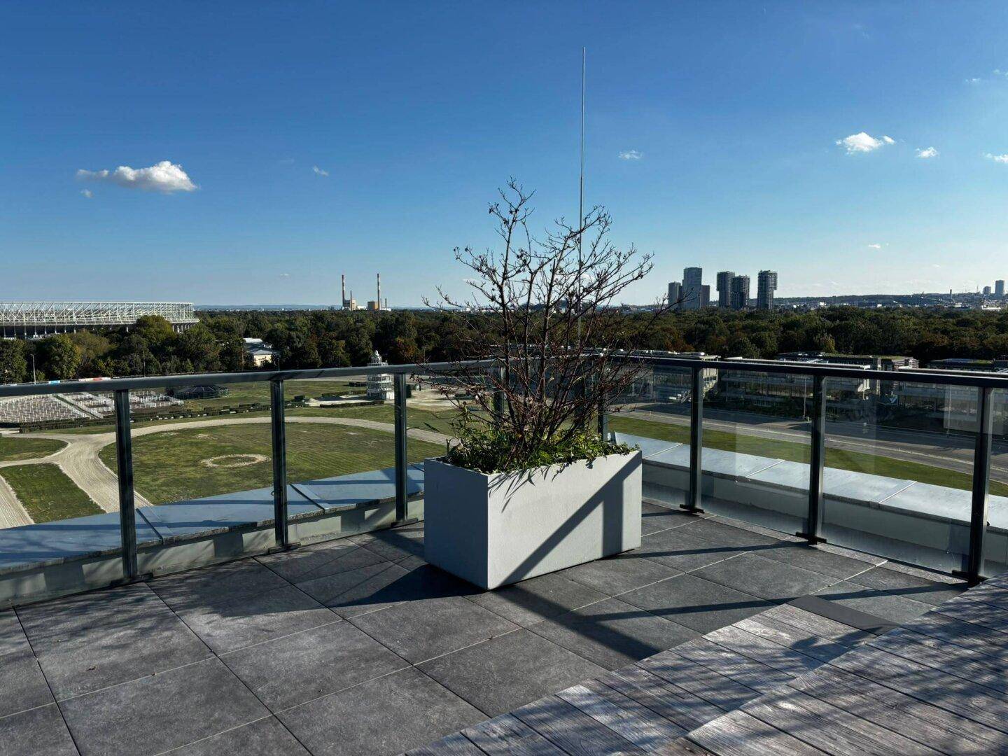 Geräumige Dachterrasse mit Glasgeländer und weitem Blick auf ein Stadion und die Skyline.
