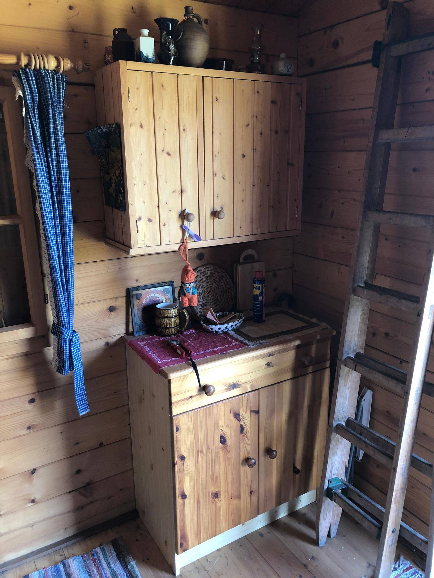 Rustikaler Schrankbereich aus Holz mit kleinen Vorhängen und Leiter in einem Holzhaus.
