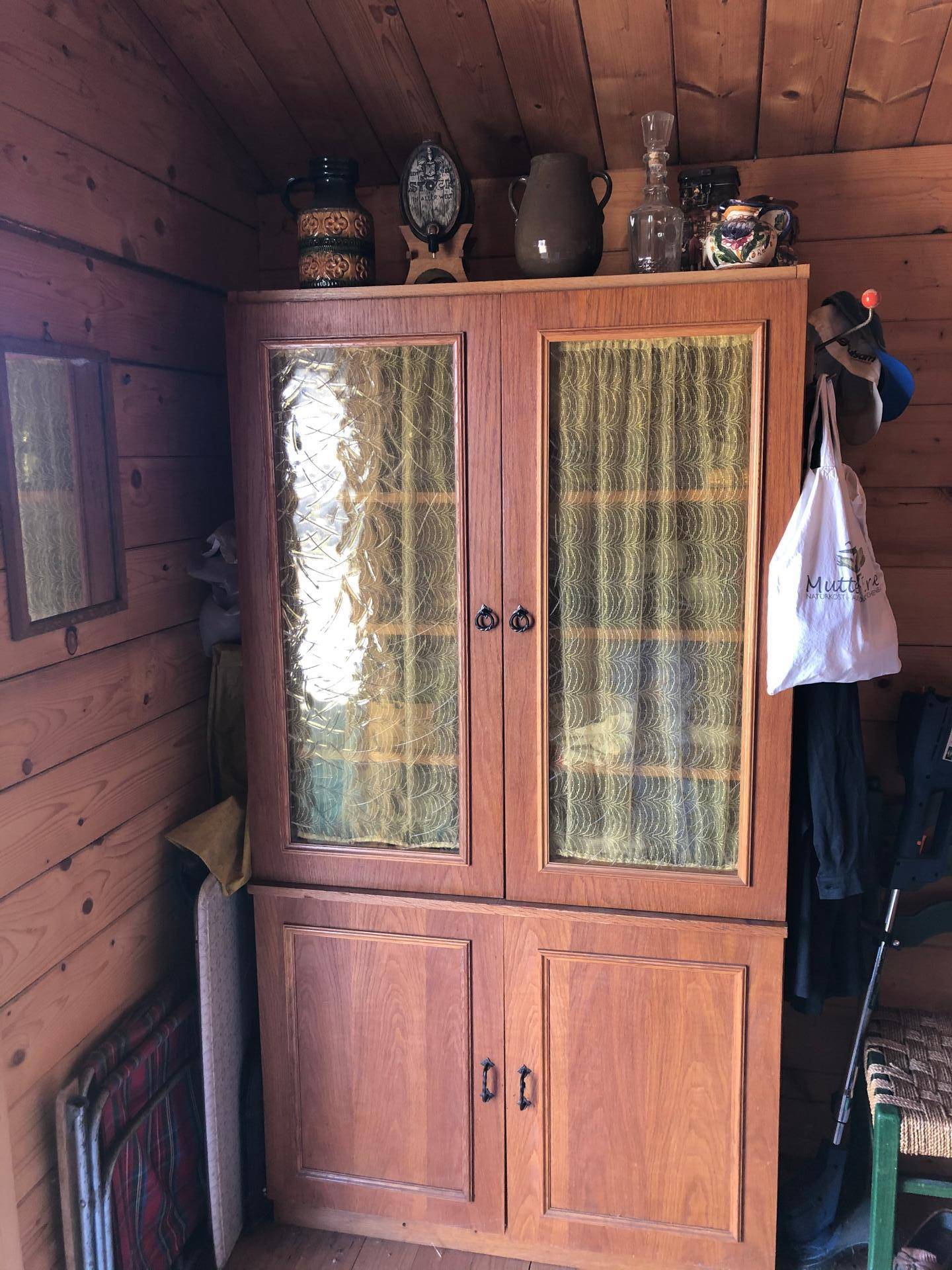 Großer Holzschrank mit Glastüren und traditionellen Dekorationen in einem rustikalen Raum.