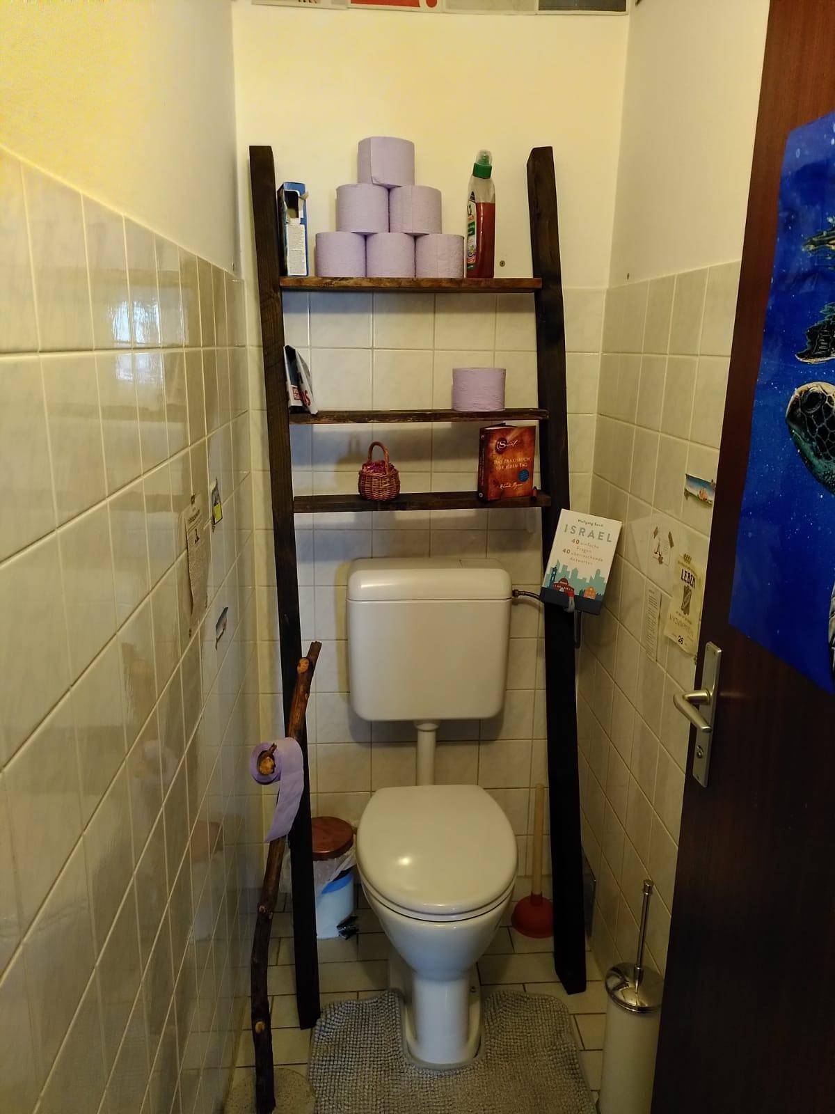 Kleines WC mit Toilette und einem dekorativen Holzregal für zusätzlichen Stauraum.