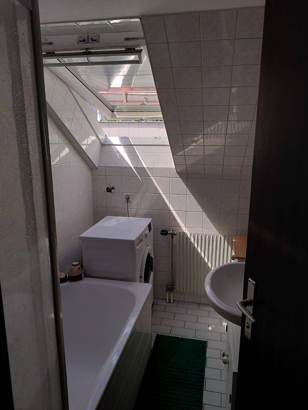 Helles Badezimmer im Dachgeschoss mit Badewanne, Waschmaschine und großem Dachfenster.