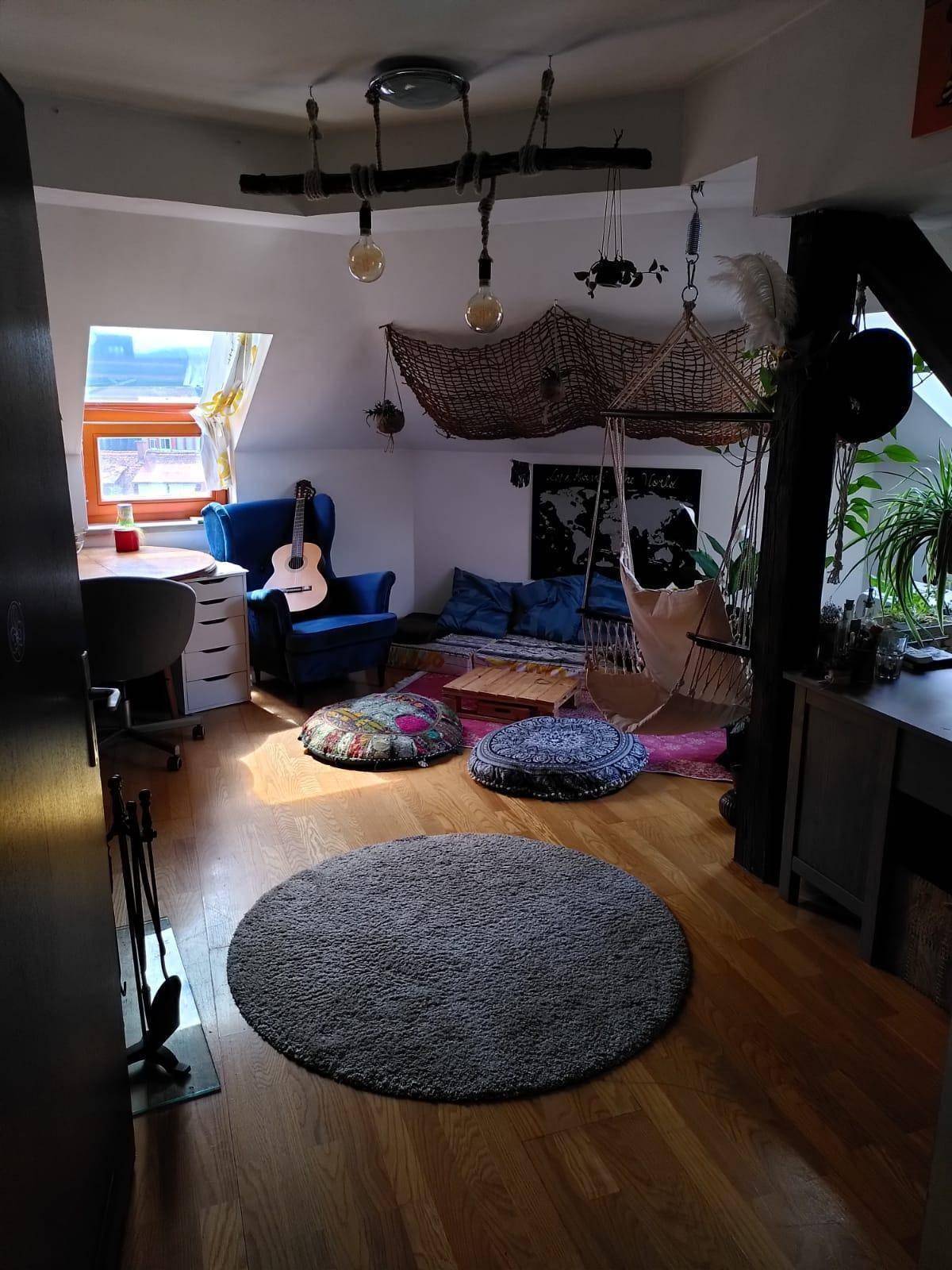 Kreativ eingerichteter Dachbodenraum mit blauer Sitzecke, Gitarre und einem großen Dachfenster für Tageslicht.