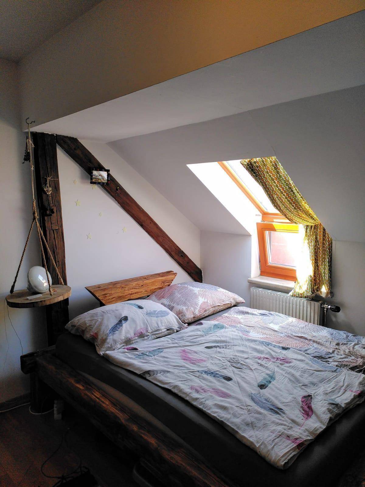 Gemütliches Schlafzimmer im Dachgeschoss mit Holzbalken, Bett und einem Dachfenster für natürliches Licht.