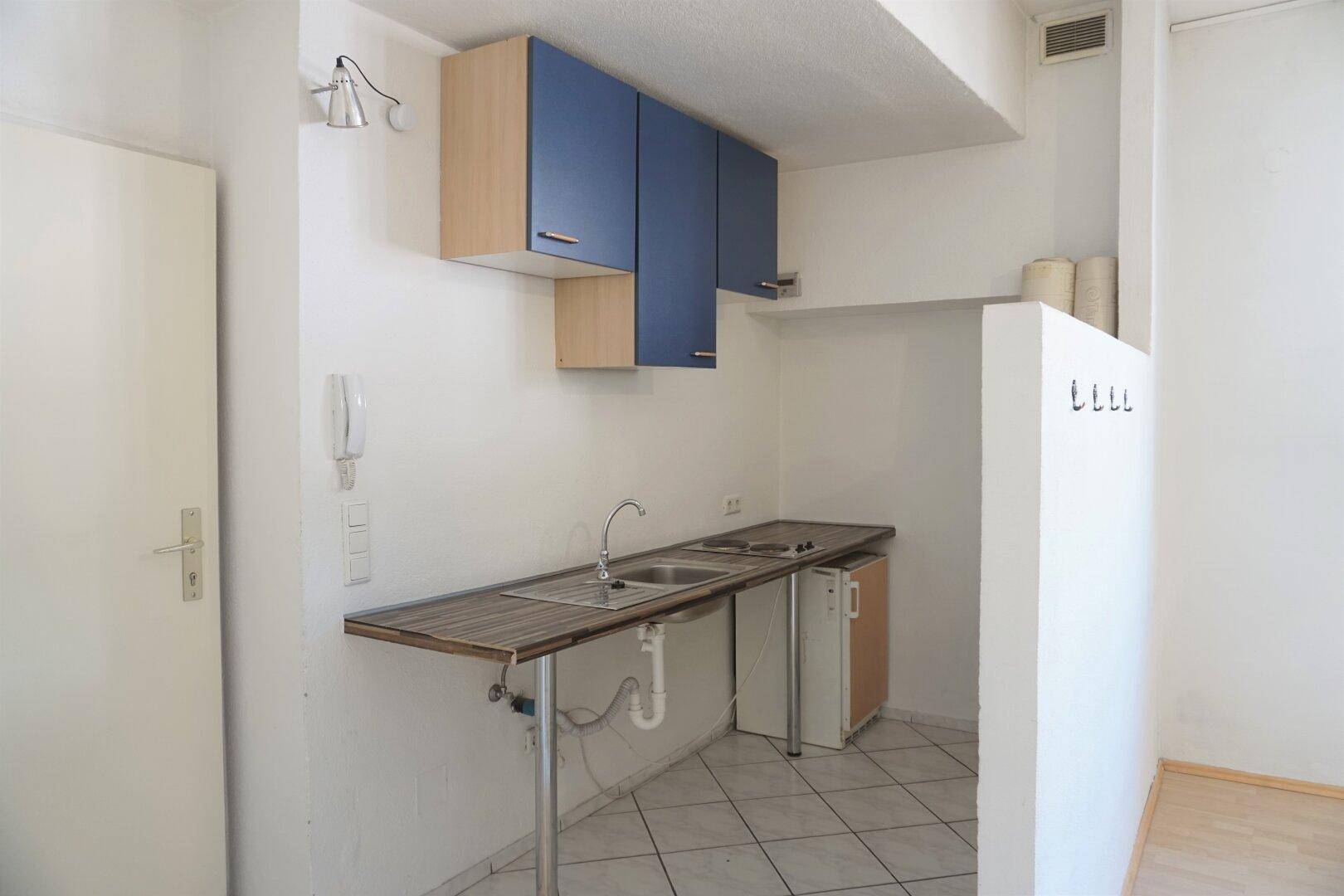 Kompakte Küchenzeile mit blauen Oberschränken, Spüle und Kühlschrank, ideal für kleine Wohn- oder Büroeinheiten.