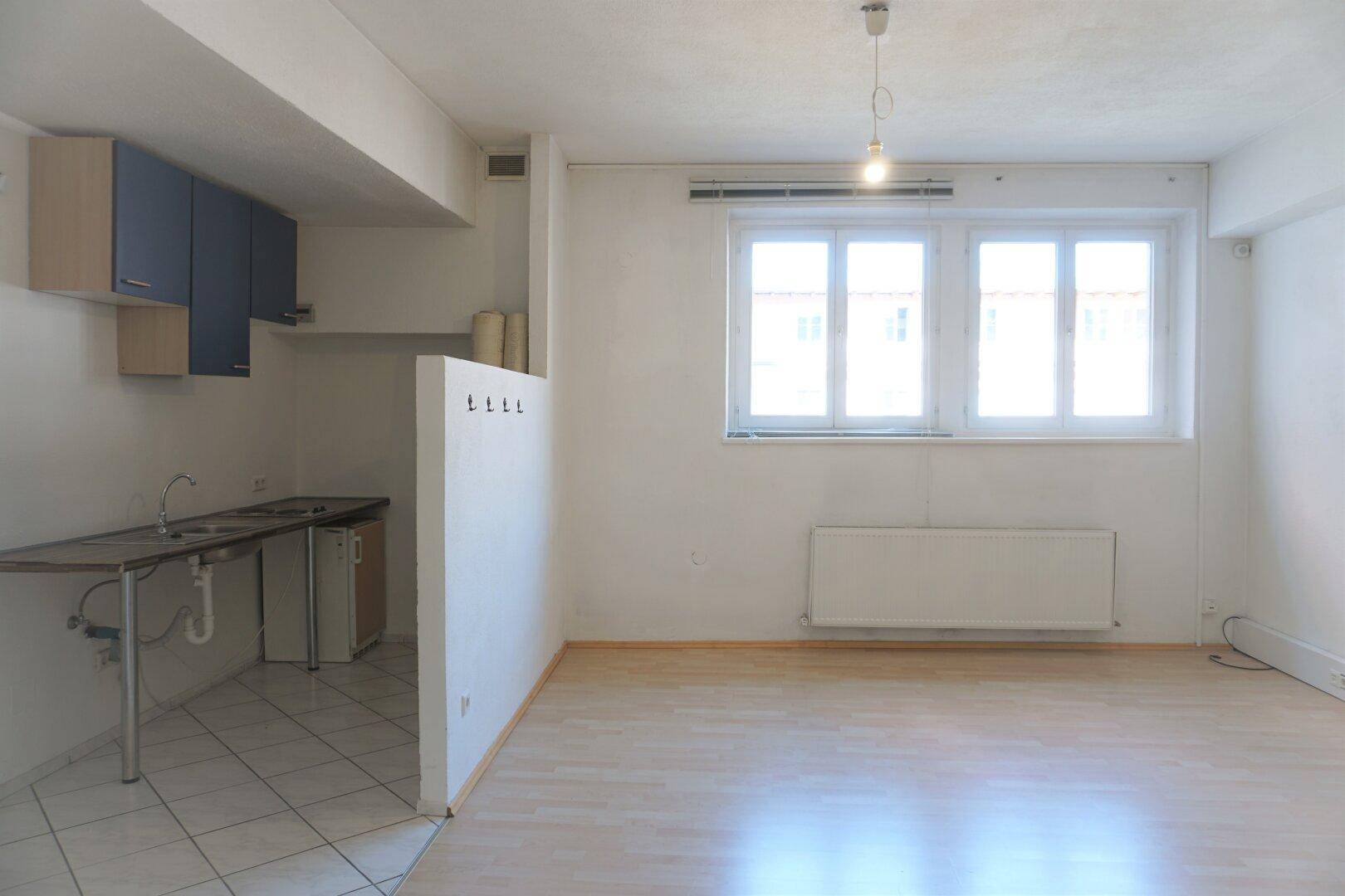 Kombinierter Raum mit Küchenzeile und hellem Holzboden, großen Fenstern und viel Tageslicht, vielseitig nutzbar.