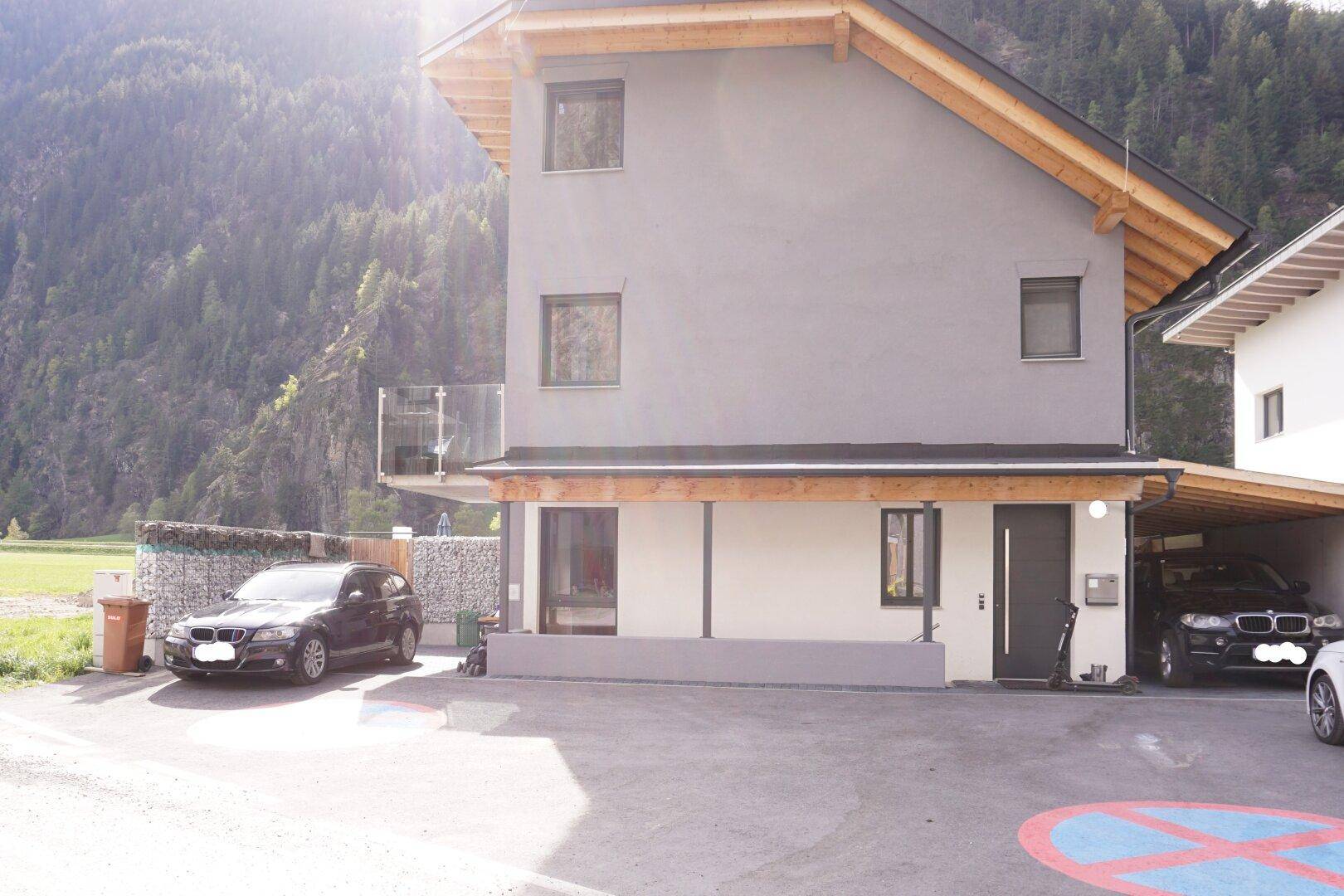 Seitenansicht des modernen Gebäudes mit Carport und Parkplätzen vor einer Bergkulisse.
