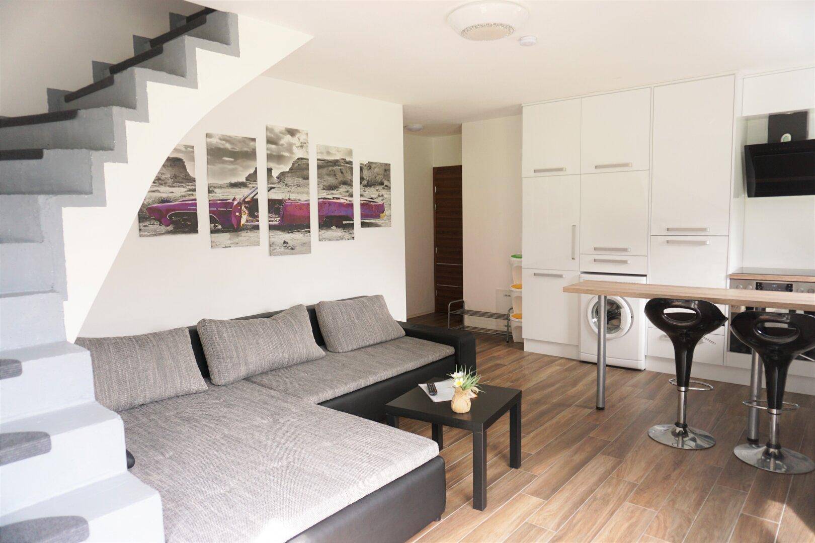 Moderner Wohnbereich mit offener Küche, Sofa und Treppe, hell und funktional gestaltet.