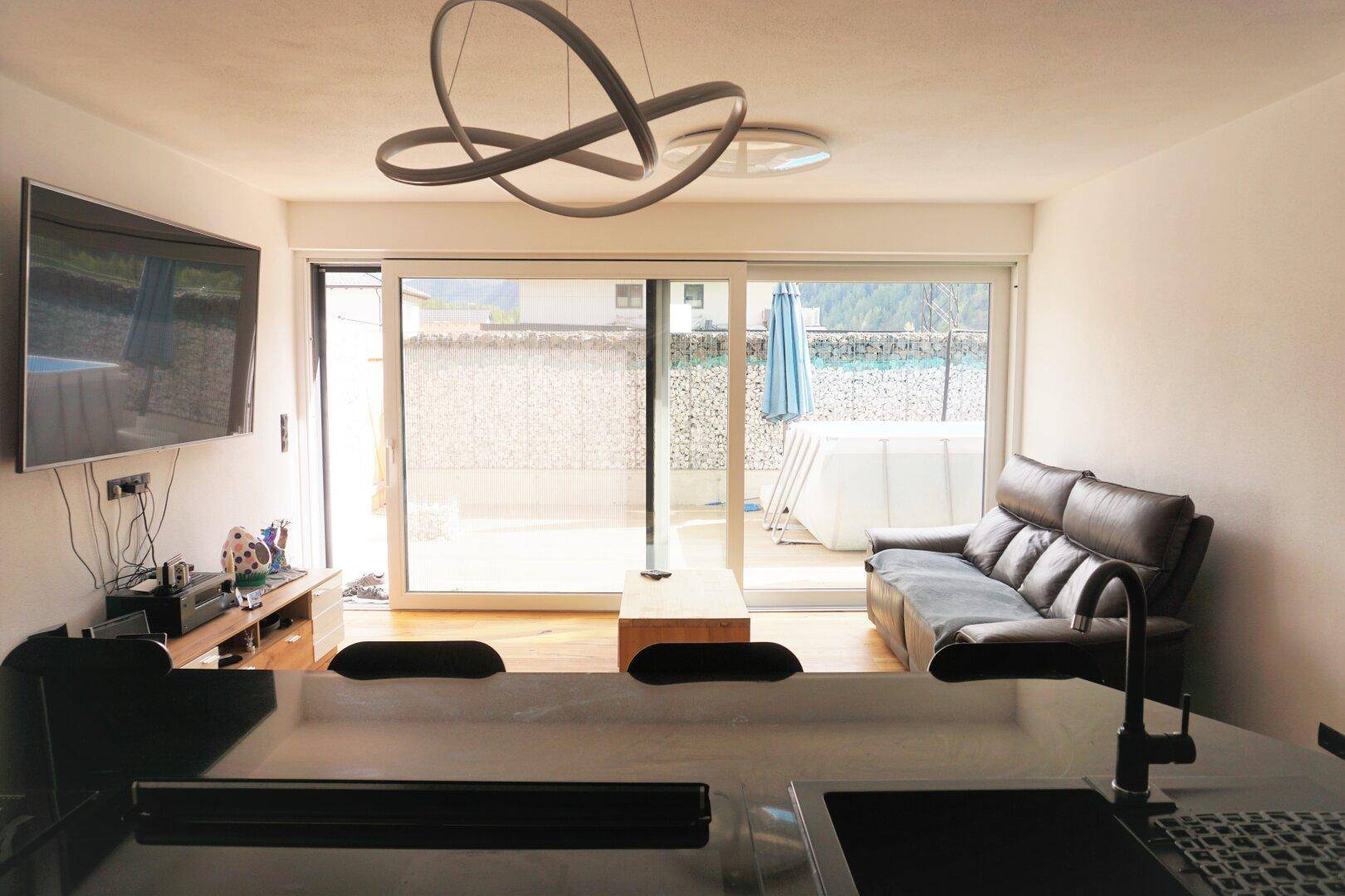 Gemütliches Wohnzimmer mit Holzboden, Sofa und Zugang zu einer Terrasse mit kleinem Pool.