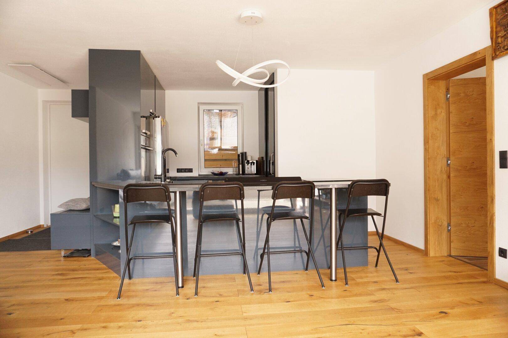 Moderne Küche mit dunkler Kücheninsel, Barhockern und Holzboden in offenem Wohnbereich.