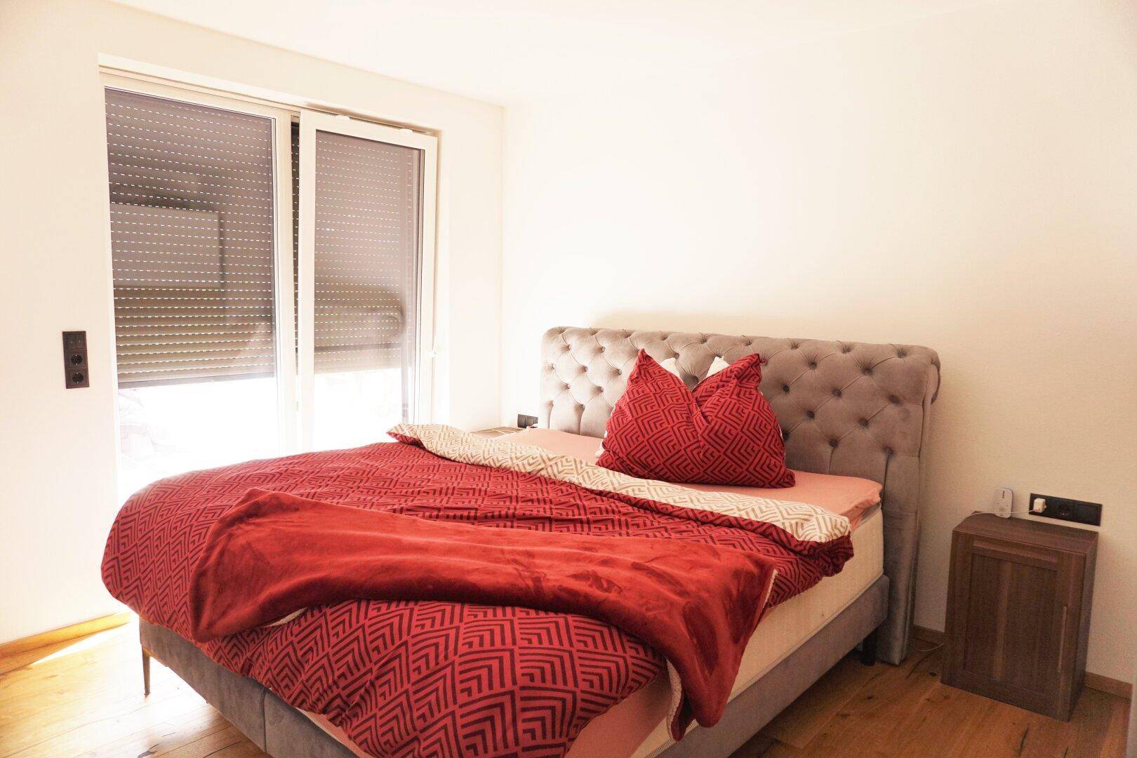 Helles Schlafzimmer mit großem Bett, Holzboden und Fenster mit Rollladen für Privatsphäre.