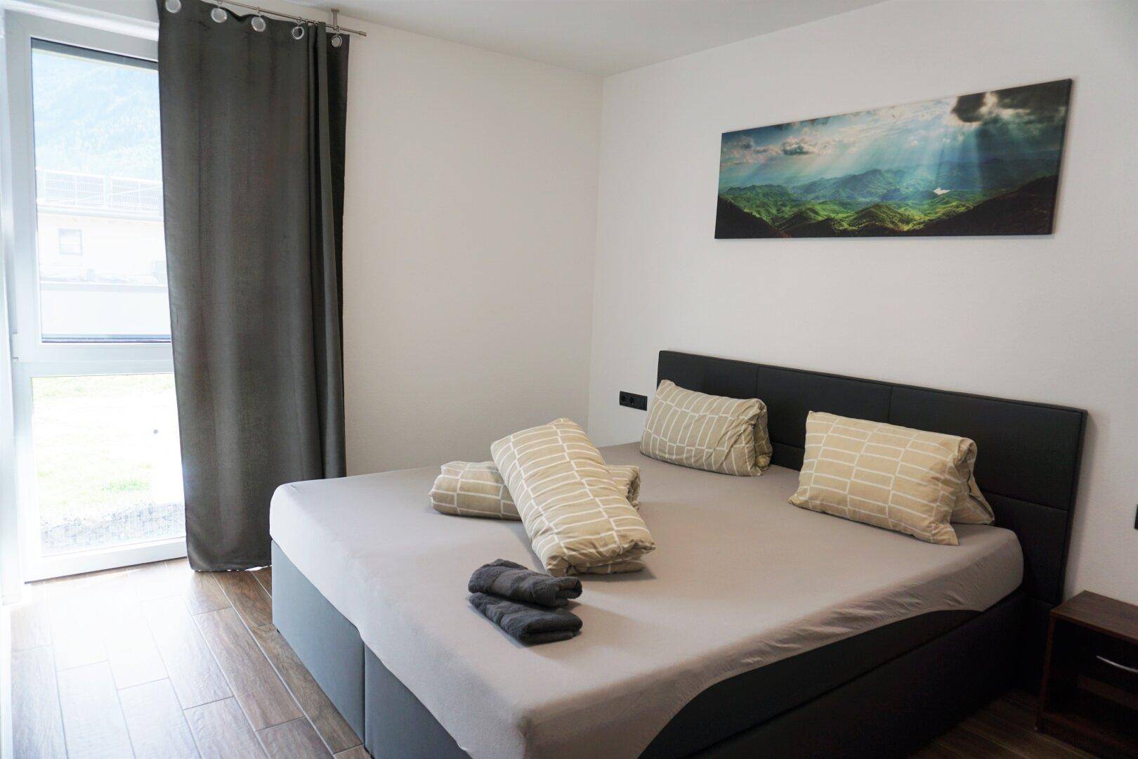 Geräumiges Schlafzimmer mit Doppelbett, Holzboden und Fenster mit Blick ins Grüne.