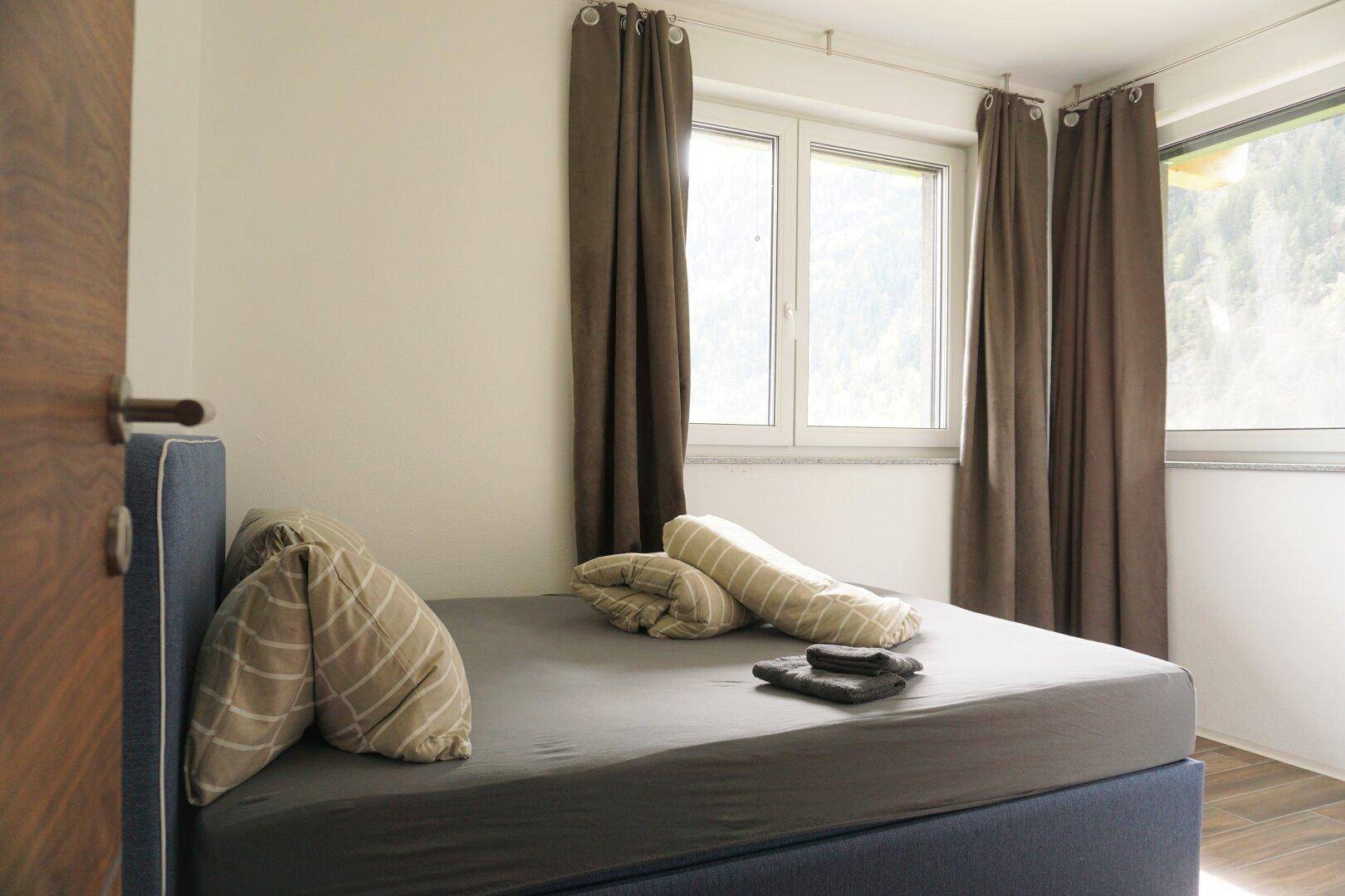 Helles Schlafzimmer mit Doppelbett, Vorhängen und Fenster mit Blick auf die umliegende Natur.
