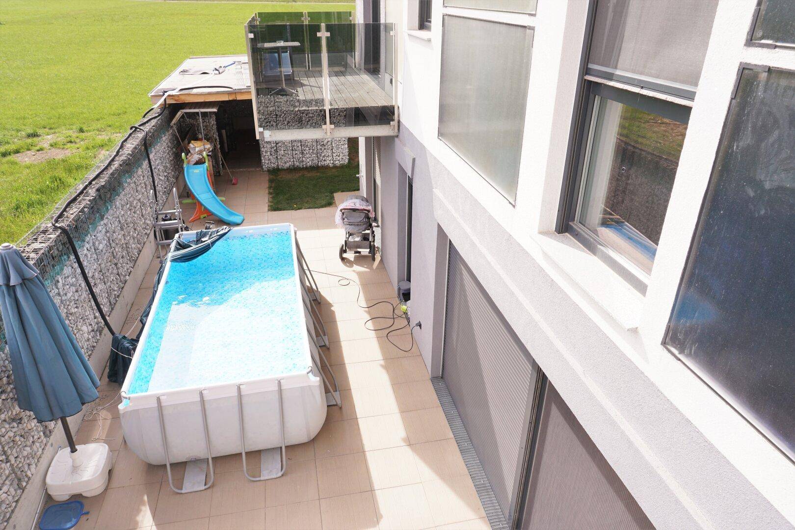 Sonniger Terrassenbereich mit kleinem Aufstellpool, Rutsche und viel Platz für Freizeitaktivitäten.