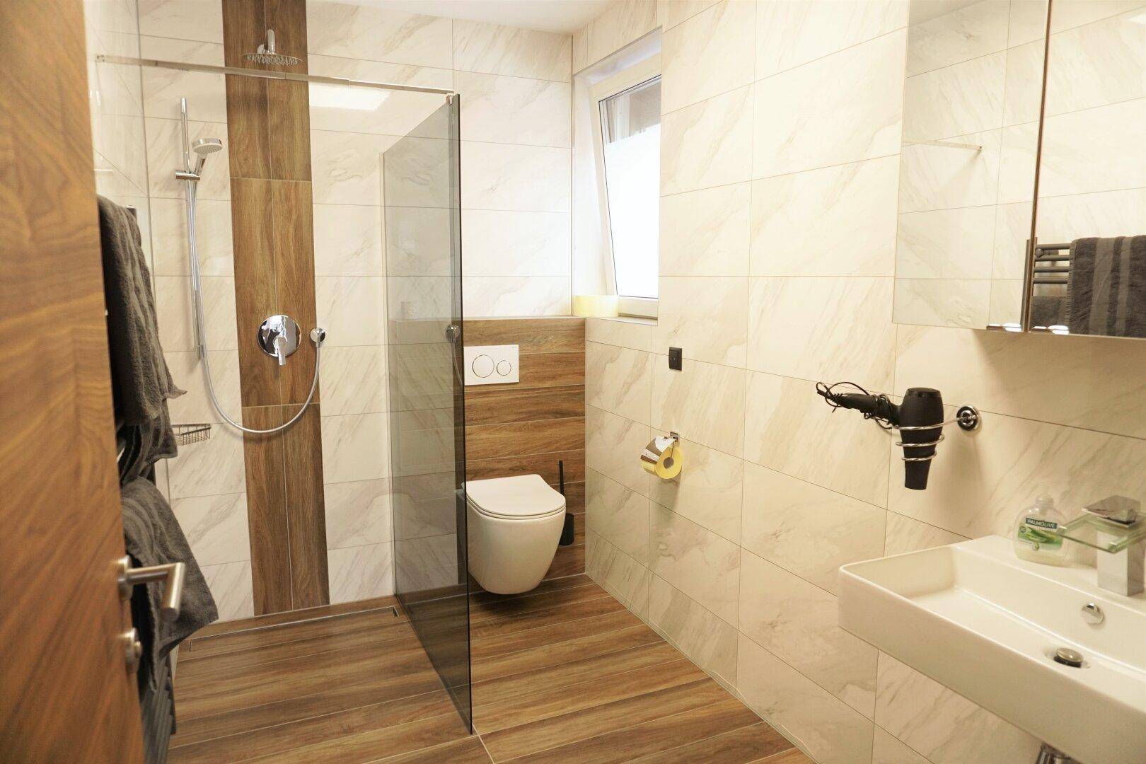 Modernes Badezimmer mit begehbarer Dusche, Wand-WC und hellen Fliesen in Holzoptik.