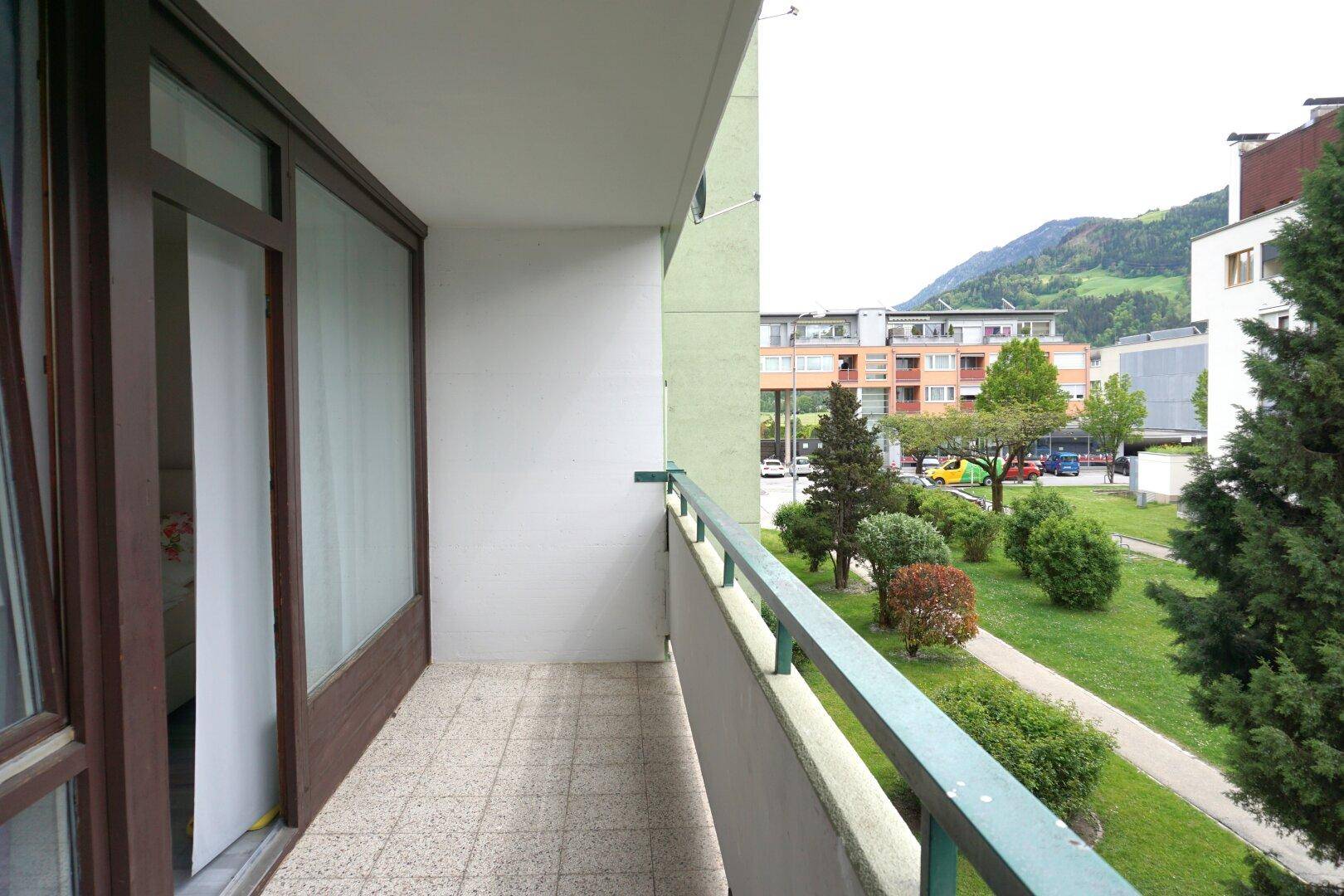 Geräumiger Balkon mit Fliesenboden und weitem Blick auf grüne Umgebung und Berge.