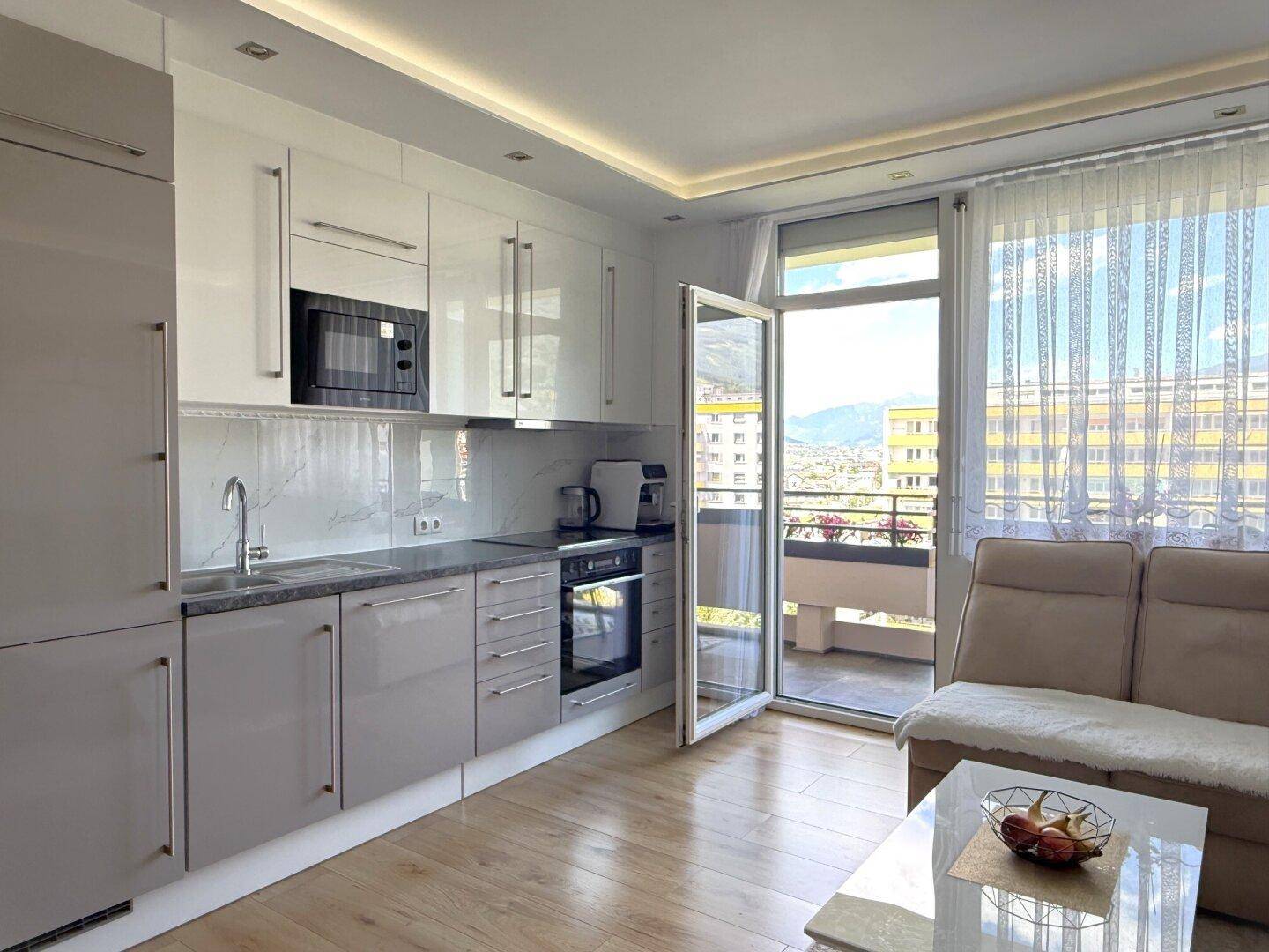 Moderne Einbauküche mit glänzenden Fronten und direktem Zugang zum Balkon.