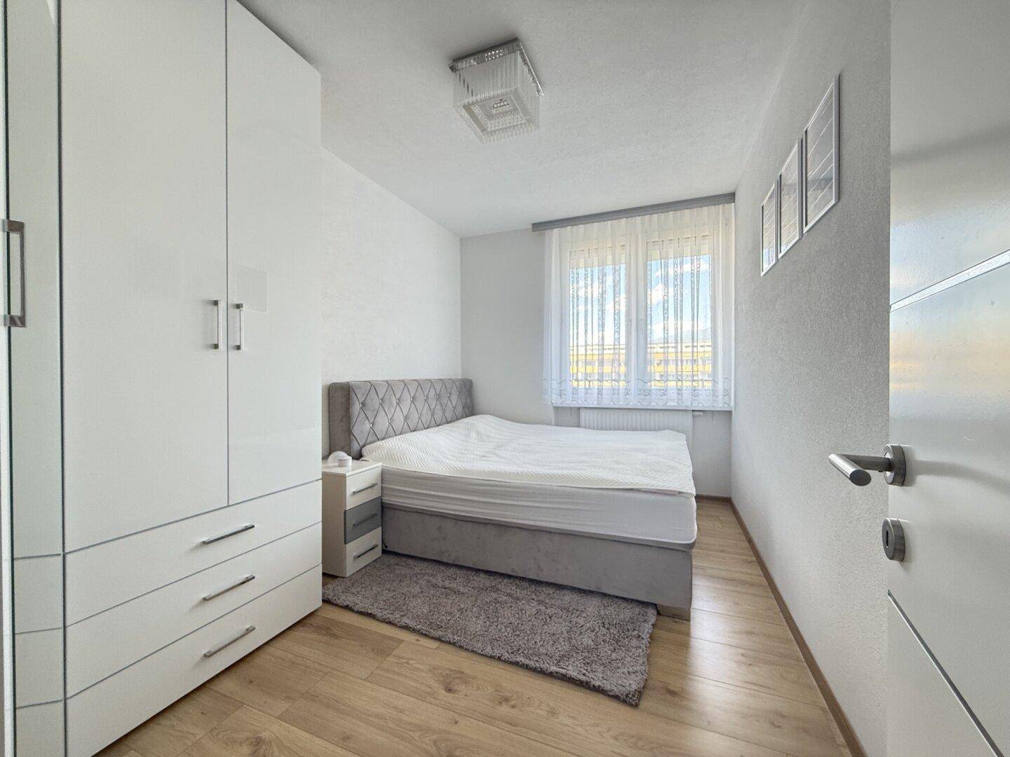Helles Schlafzimmer mit Doppelbett, Parkettboden und weißem Kleiderschrank.