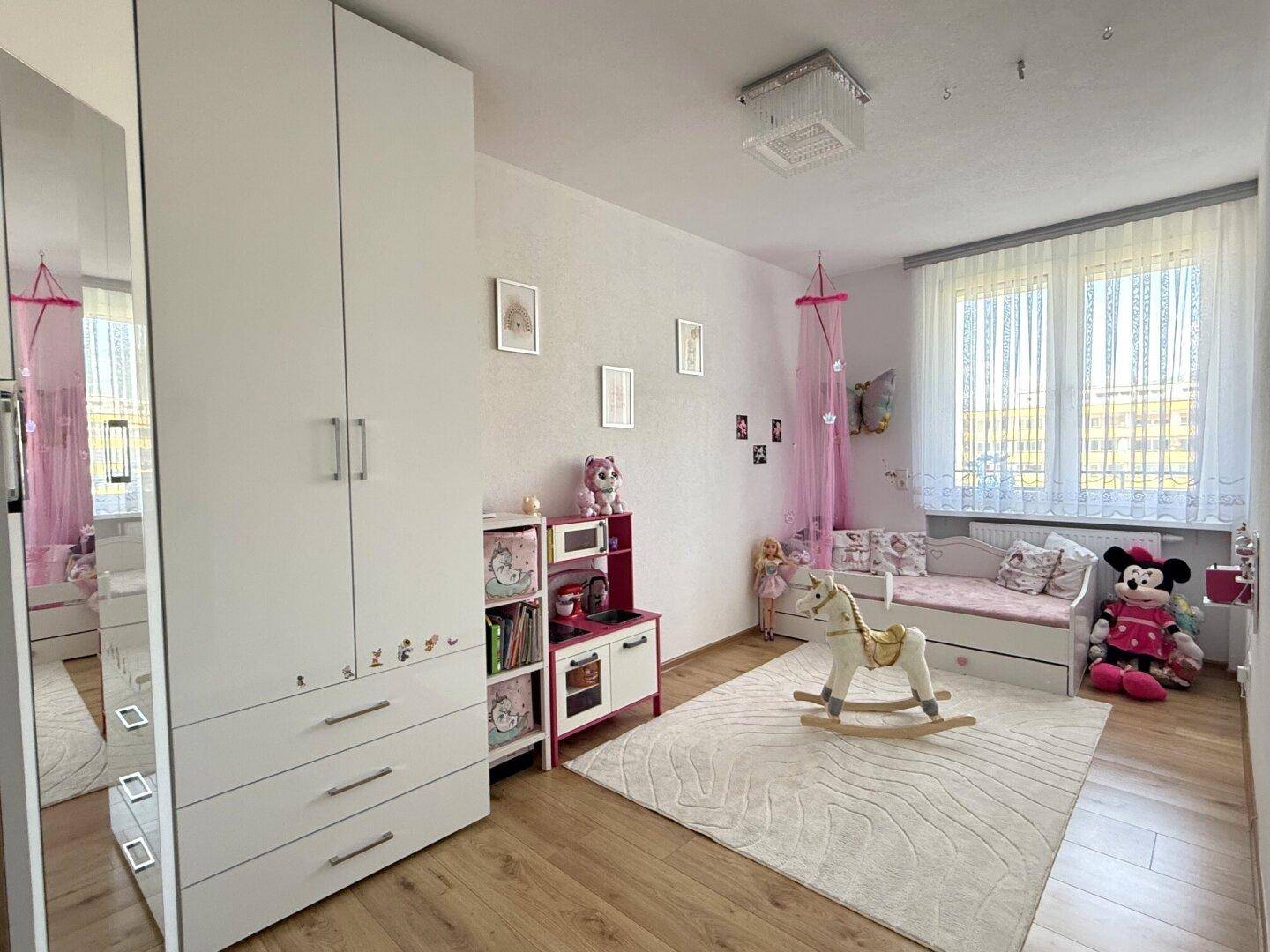 Freundliches Kinderzimmer mit Spielzeug, hellem Teppich und viel Tageslicht.