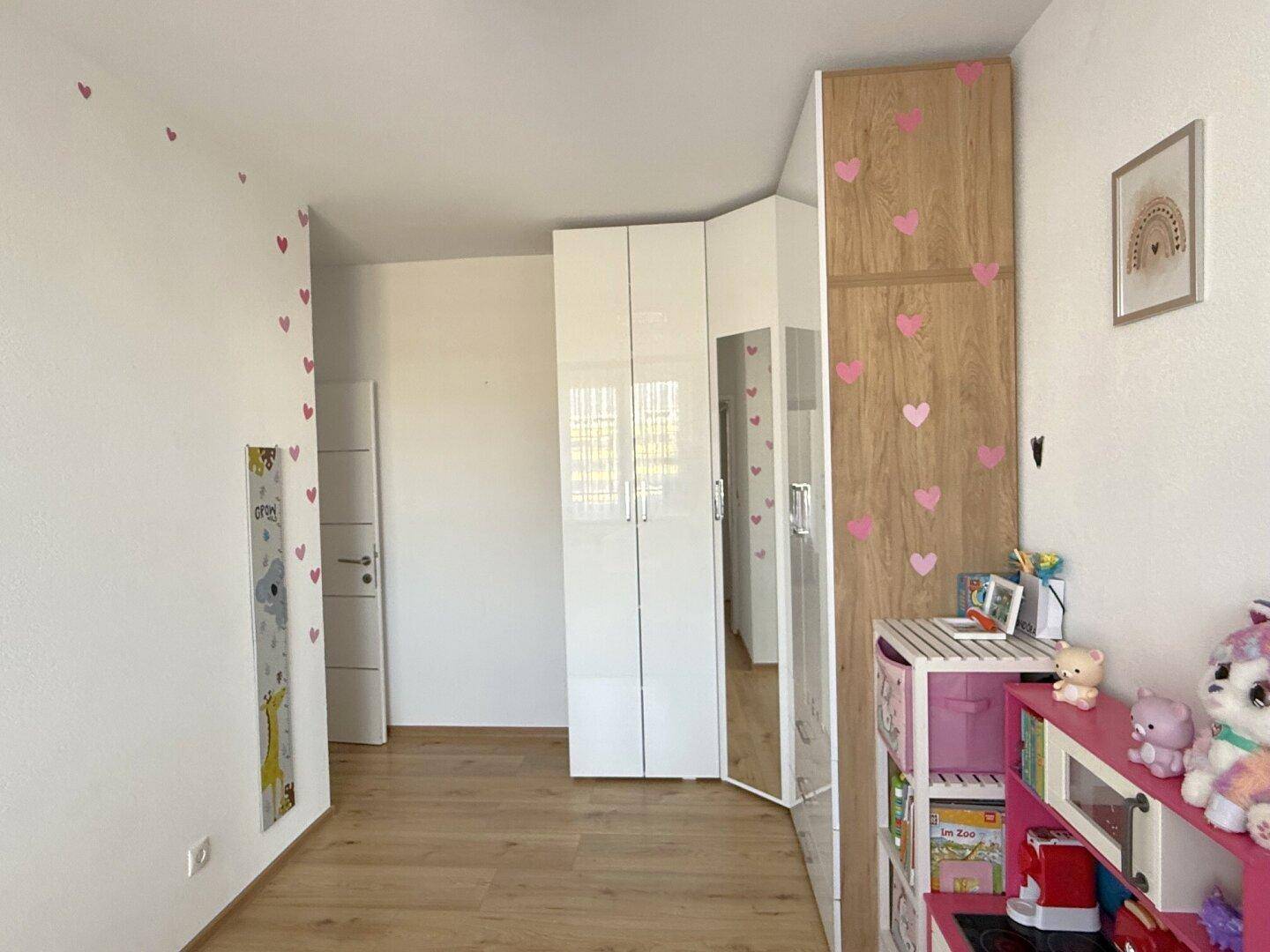 Kinderzimmer mit verspielter Dekoration, Eckkleiderschrank und Holzboden.