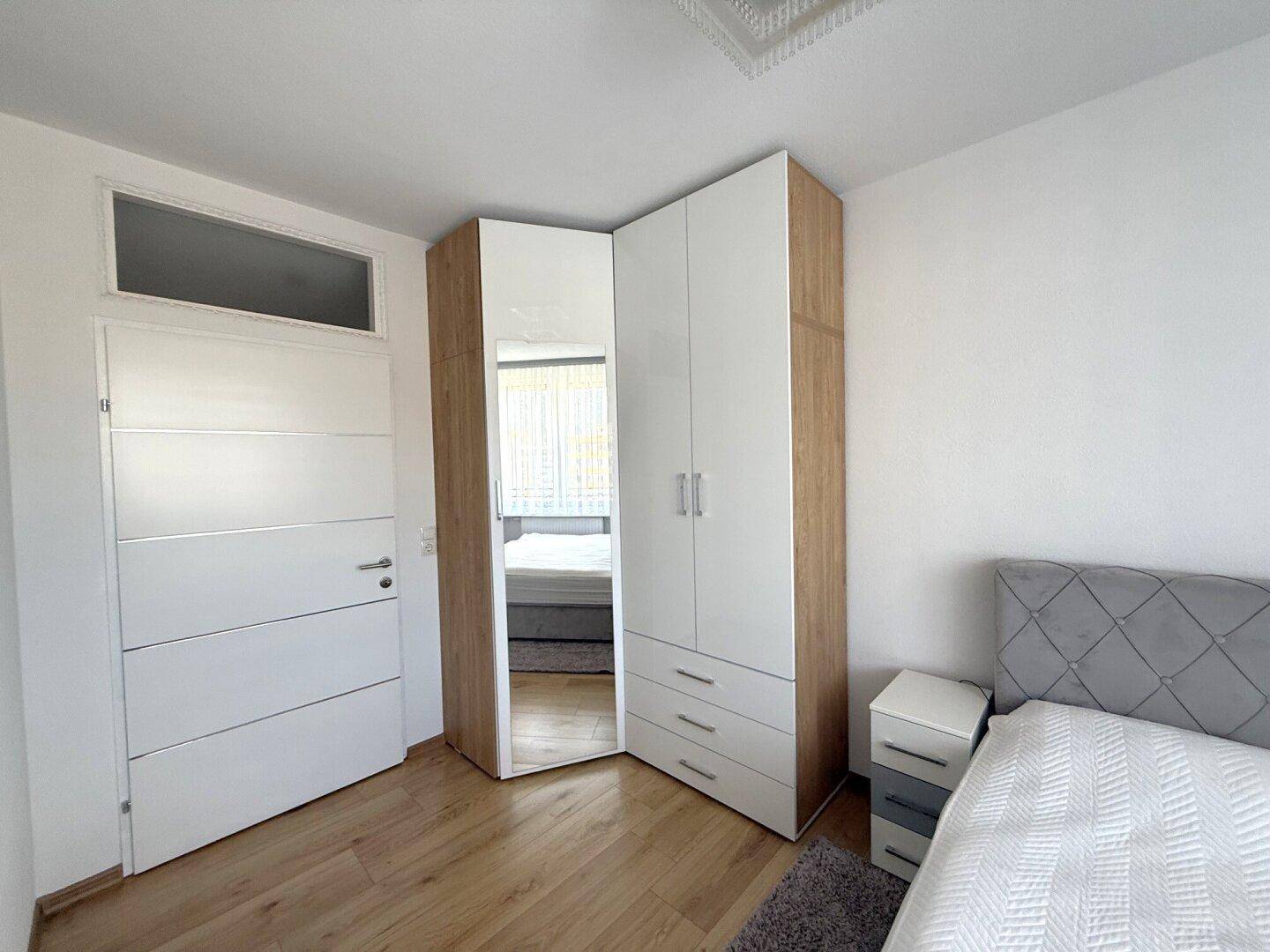 Schlafzimmer mit modernem Eckkleiderschrank und Holzboden, hell und funktional eingerichtet.