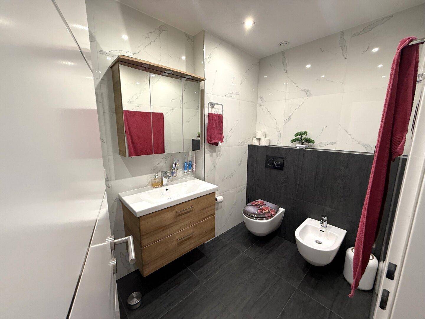 Modernes Badezimmer mit Waschtisch, WC, Bidet und eleganten Fliesen in Marmoroptik.