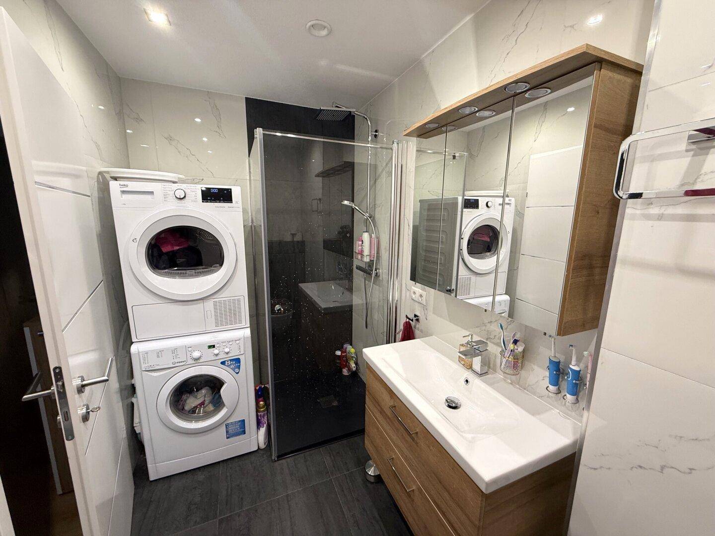Modernes Badezimmer mit Dusche, Waschtisch und integriertem Waschmaschinen-Trockner-Turm.