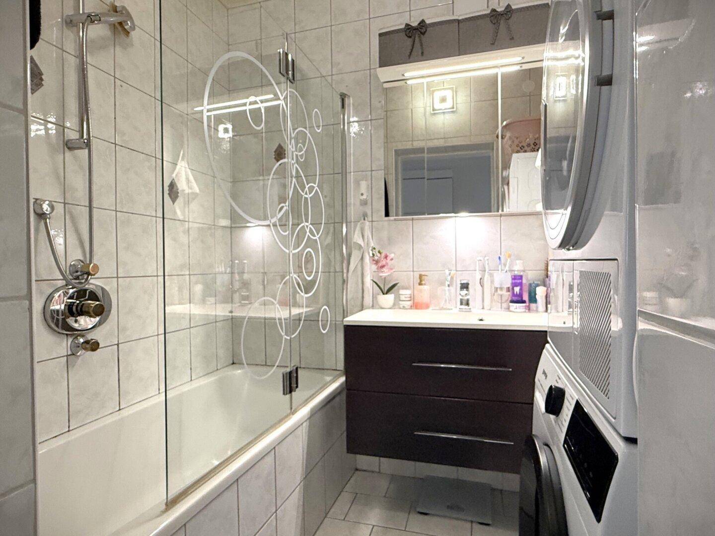 Modernes Badezimmer mit Badewanne, Duschabtrennung und integriertem Waschtrockner.