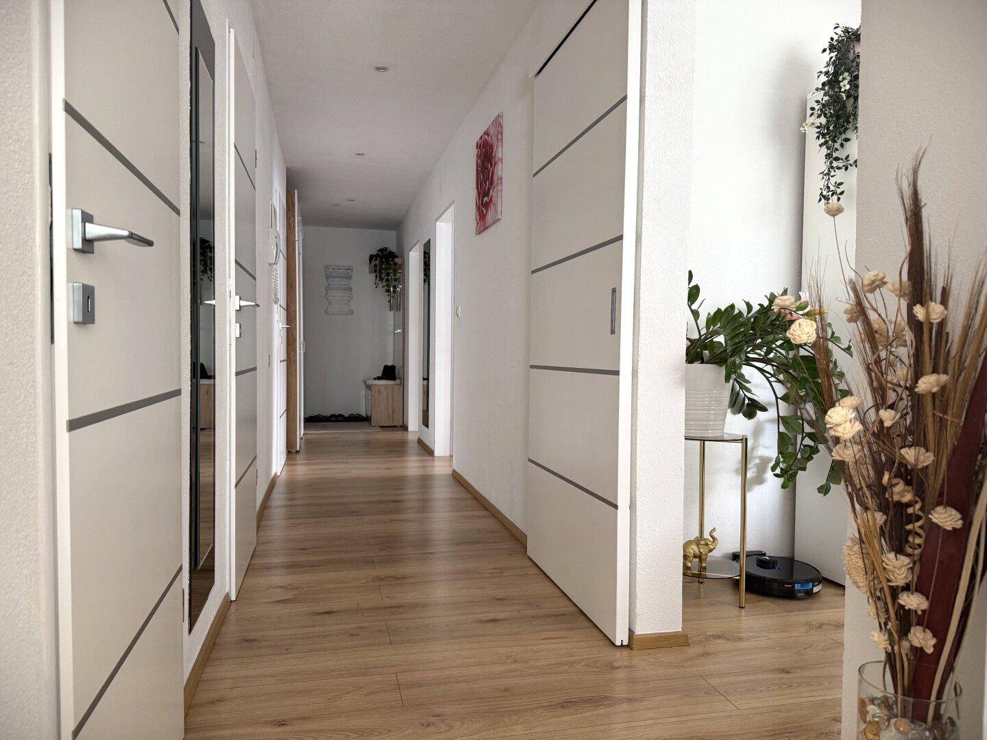 Langer, heller Flur mit Holzboden und modernen Türen, der zu den Zimmern führt.