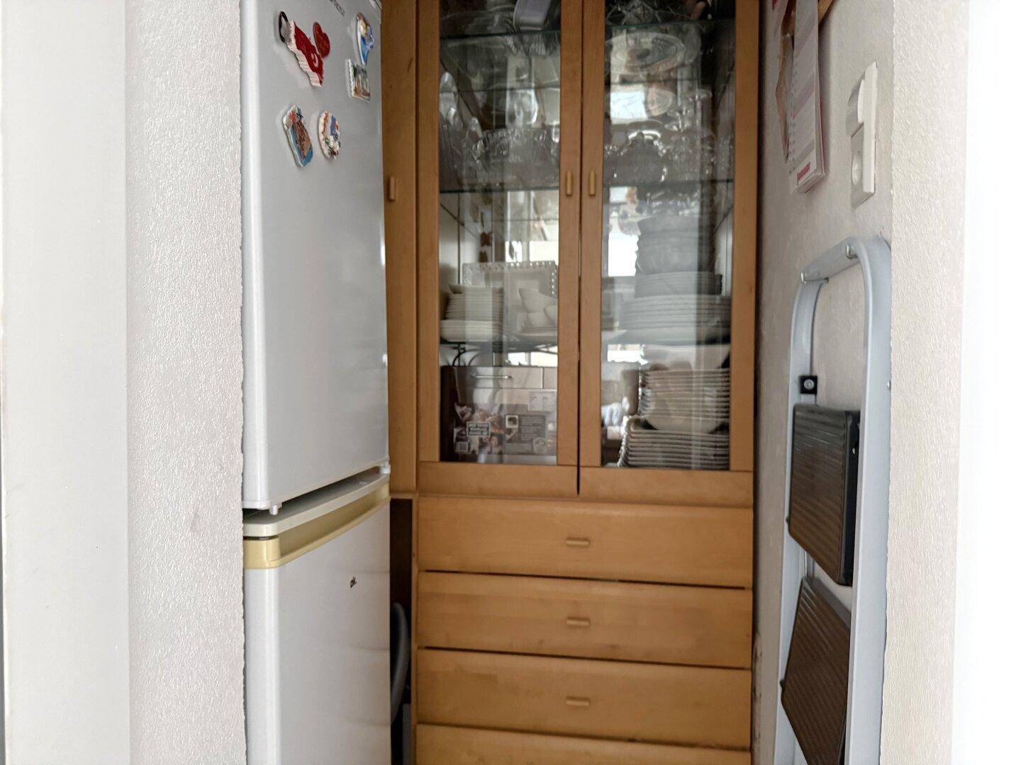Praktischer Abstellraum mit Kühlschrank und Holzschrank für zusätzlichen Stauraum.