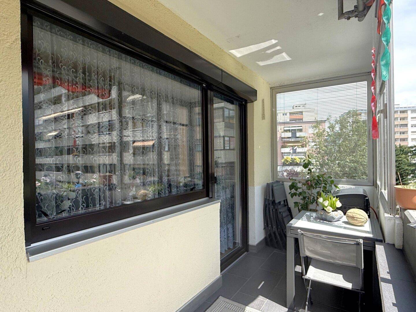 Heller Balkon mit großen Fenstern und Blick auf die Wohnanlage.