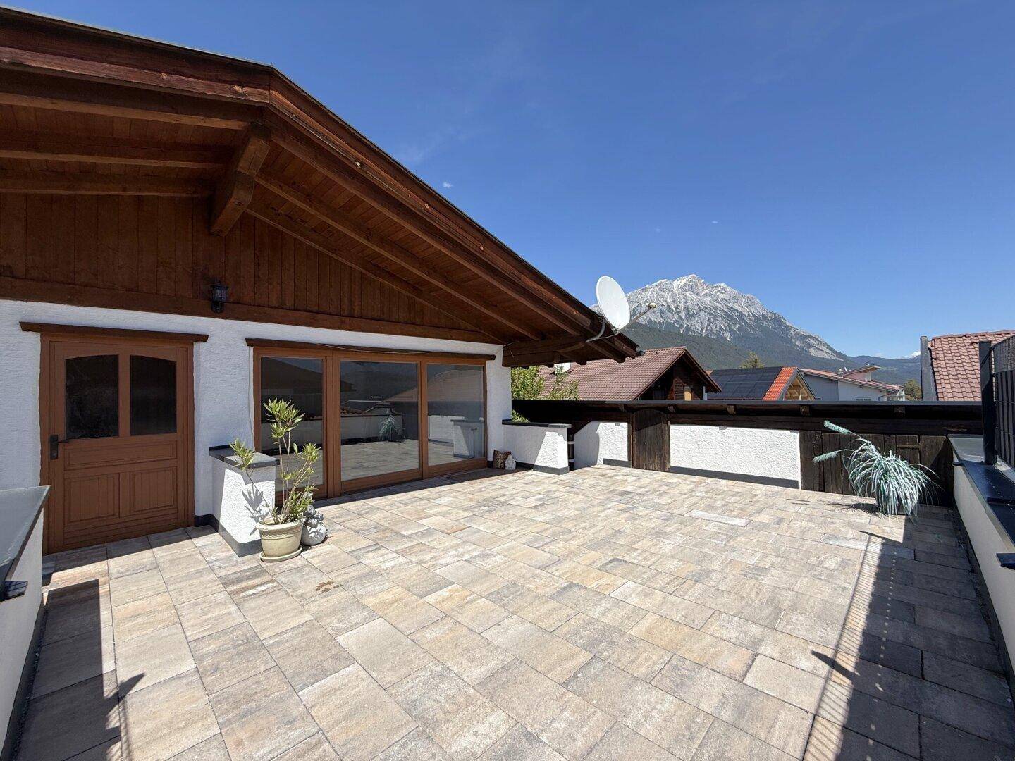 Geräumige Terrasse mit Holztür und Glasfronten, die einen direkten Blick auf die majestätischen Berge bietet.
