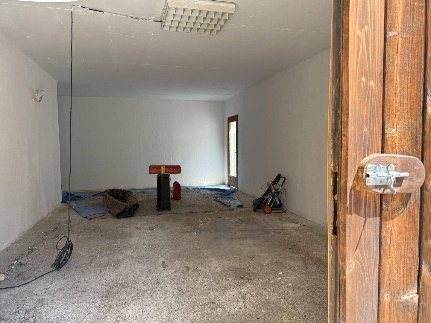 Geräumige Garage mit Betonboden und Holztüren, die als Abstellraum genutzt werden kann.