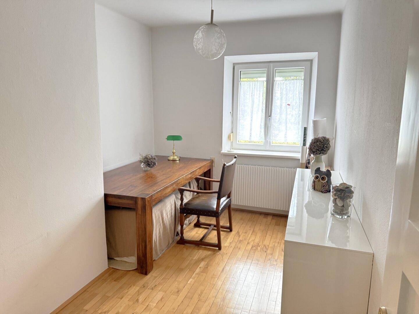 Helles Zimmer mit Holztisch, Stuhl und Fenster, ideal als Büro oder Essbereich nutzbar.