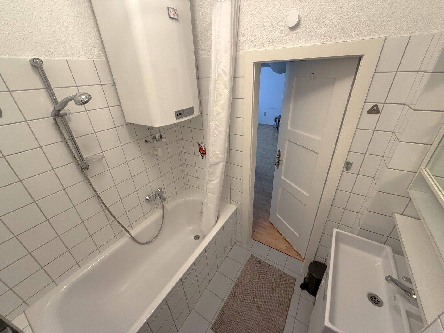 Badezimmer mit Badewanne und Duschvorrichtung, weißen Fliesen und Waschbecken.