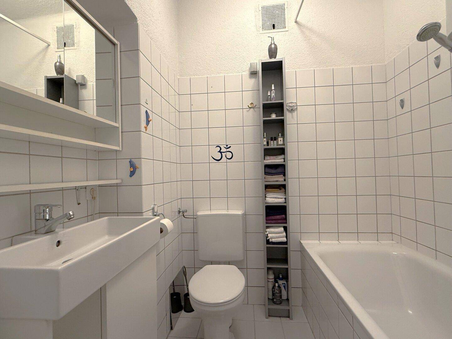 Badezimmer mit weißen Fliesen, Badewanne, WC und Waschbecken, funktional eingerichtet.