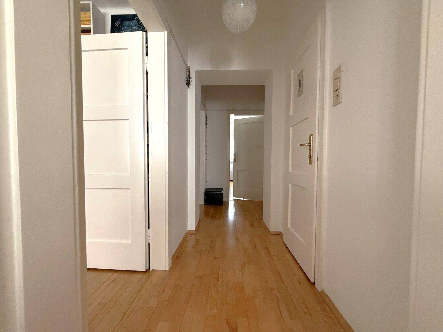 Heller Flur mit Holzboden und weißen Türen, der zu verschiedenen Räumen führt.