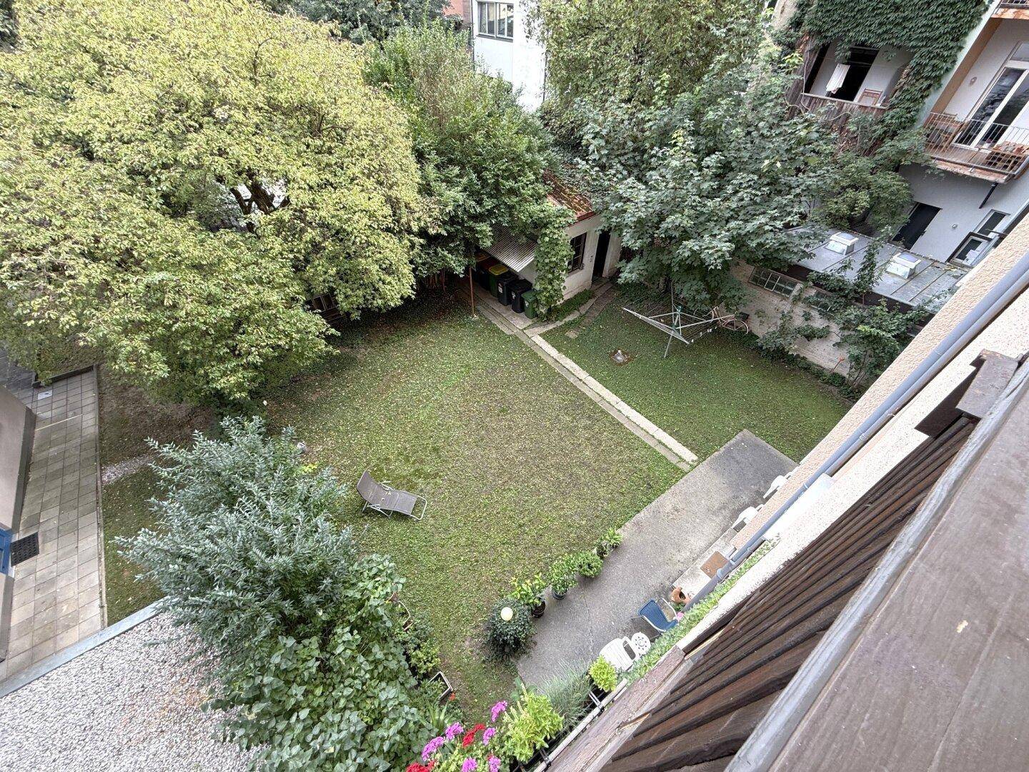 Blick von oben auf einen grünen Gemeinschaftsgarten mit Rasenfläche und Bäumen.