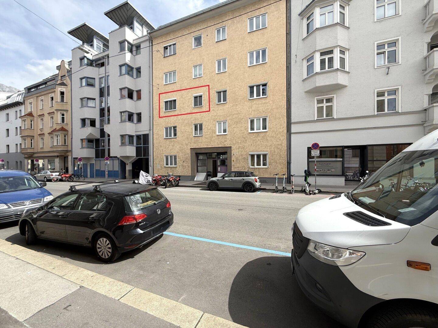 Mehrstöckiges Wohngebäude in einer städtischen Umgebung mit parkenden Autos auf der Straße.