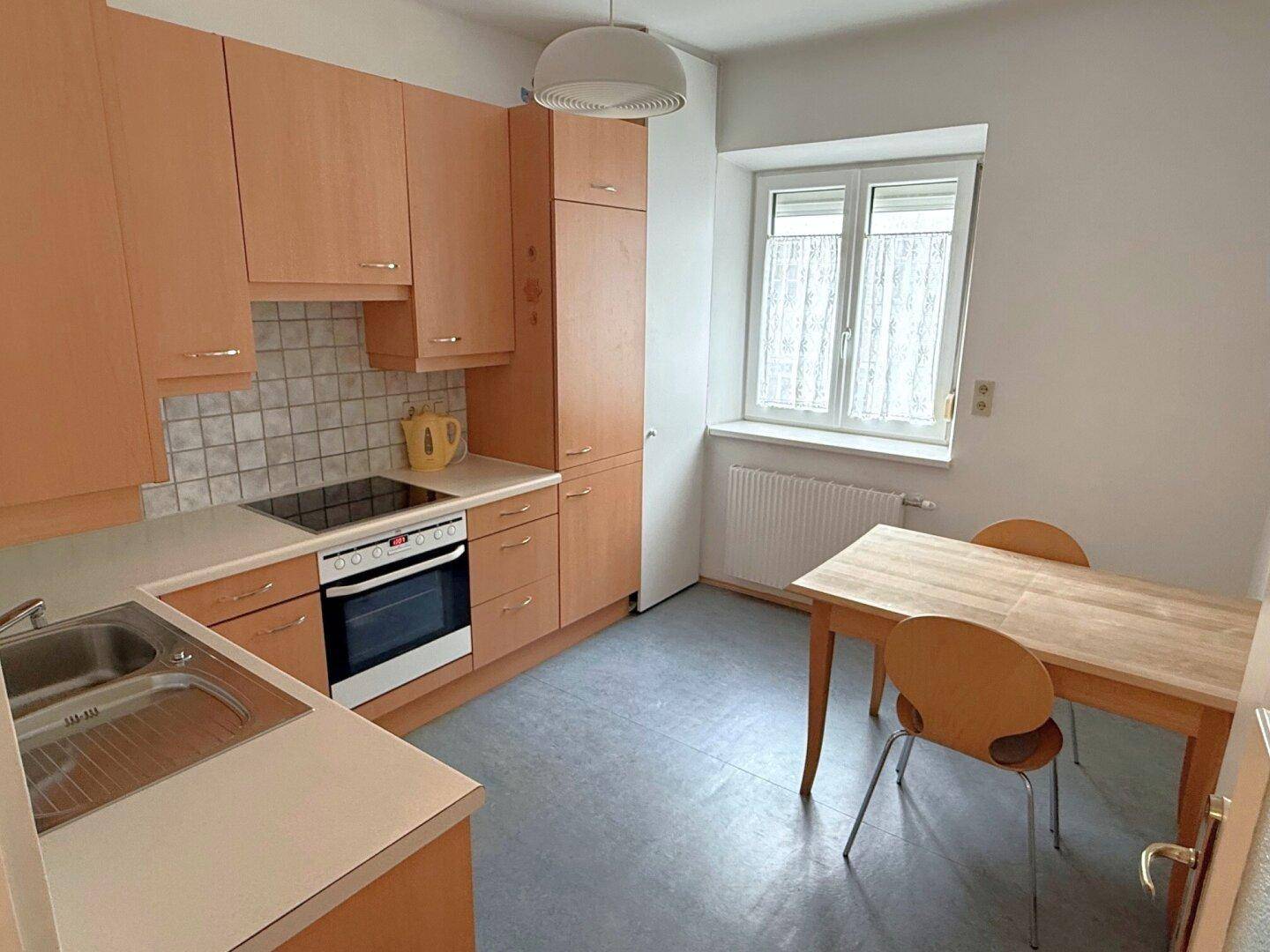Funktionale Küche mit hellen Holzschränken, Essbereich und Fenster, gut ausgestattet.