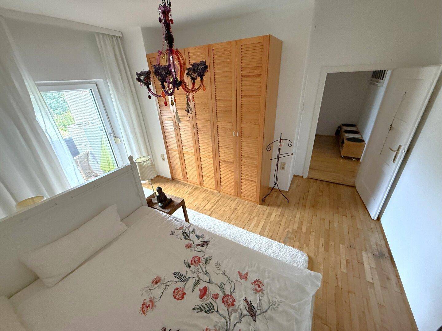 Schlafzimmer mit Holzboden, großem Kleiderschrank und Zugang zu einem Außenbereich.