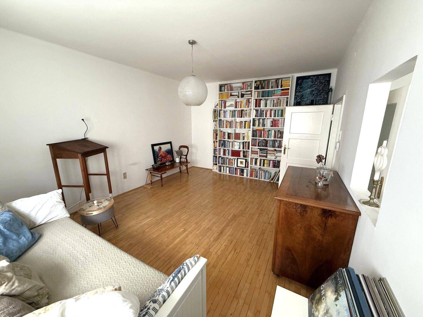 Gemütliches Wohnzimmer mit Tagesbett, Bücherregal und Holzboden, hell und einladend.