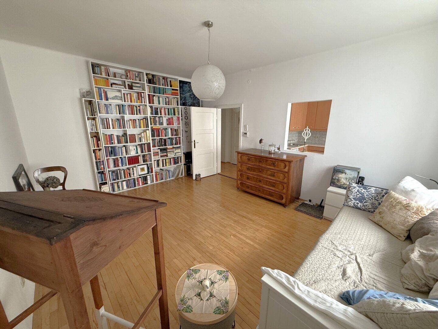 Wohnzimmer mit großer Bücherwand, Holzboden und einem Durchgang zur Küche.