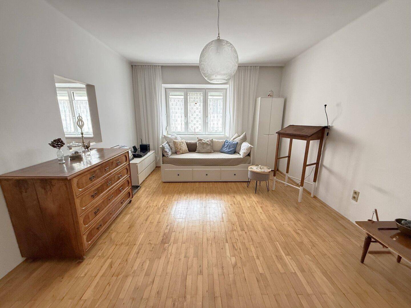 Geräumiges Wohnzimmer mit Holzboden, Tagesbett und einem großen Fenster, das viel Licht hereinlässt.