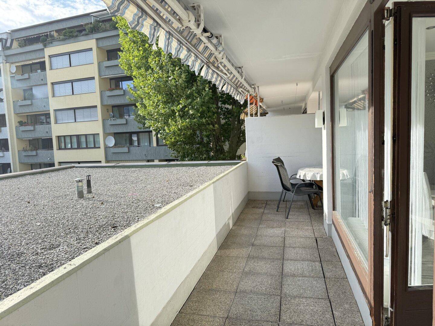 Heller Balkon mit Markise, Fliesenboden und Sitzgelegenheiten mit Blick auf die Umgebung.