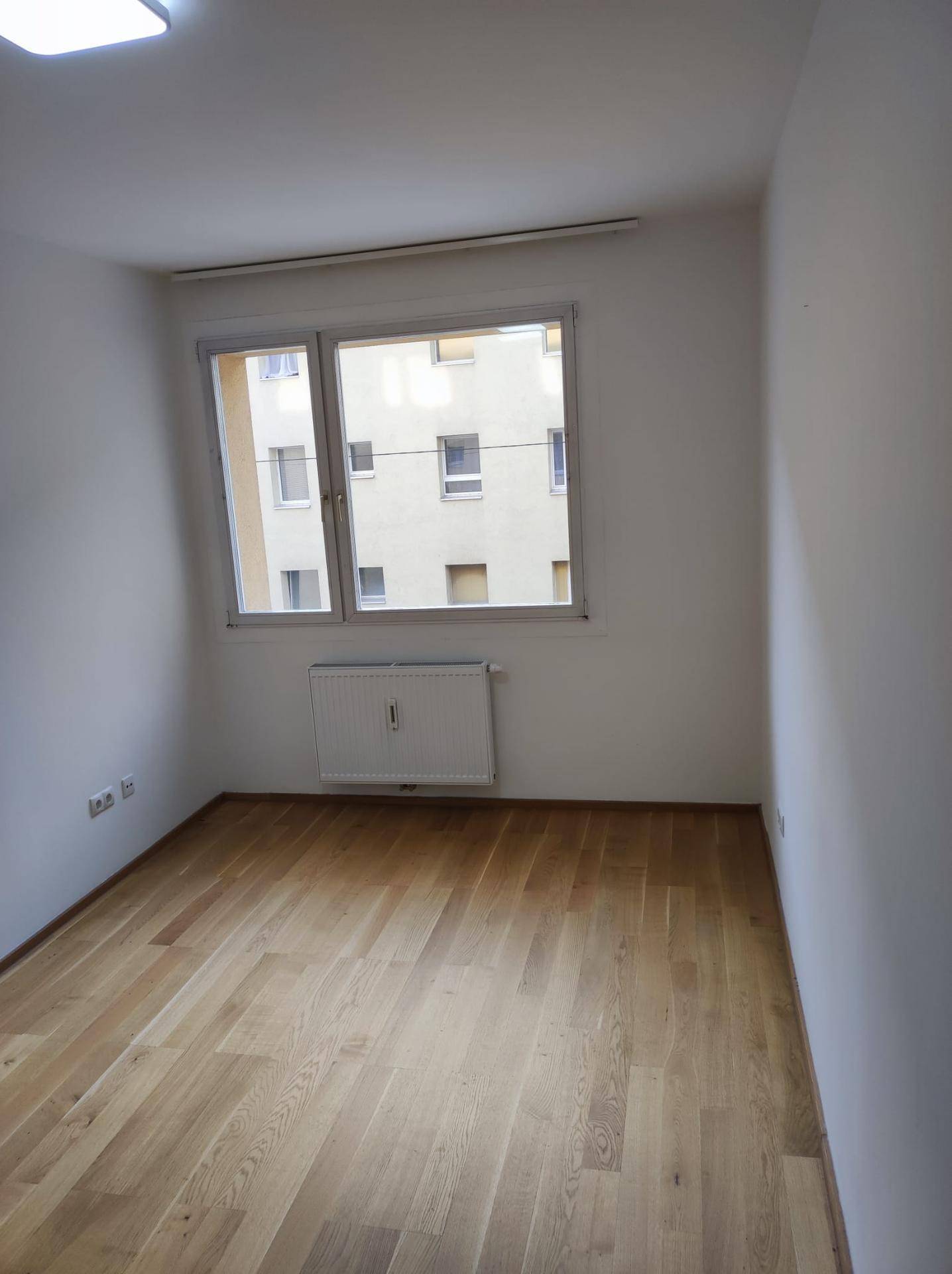 Heller Raum mit Parkettboden und einem großen Fenster, das viel Tageslicht hereinlässt.