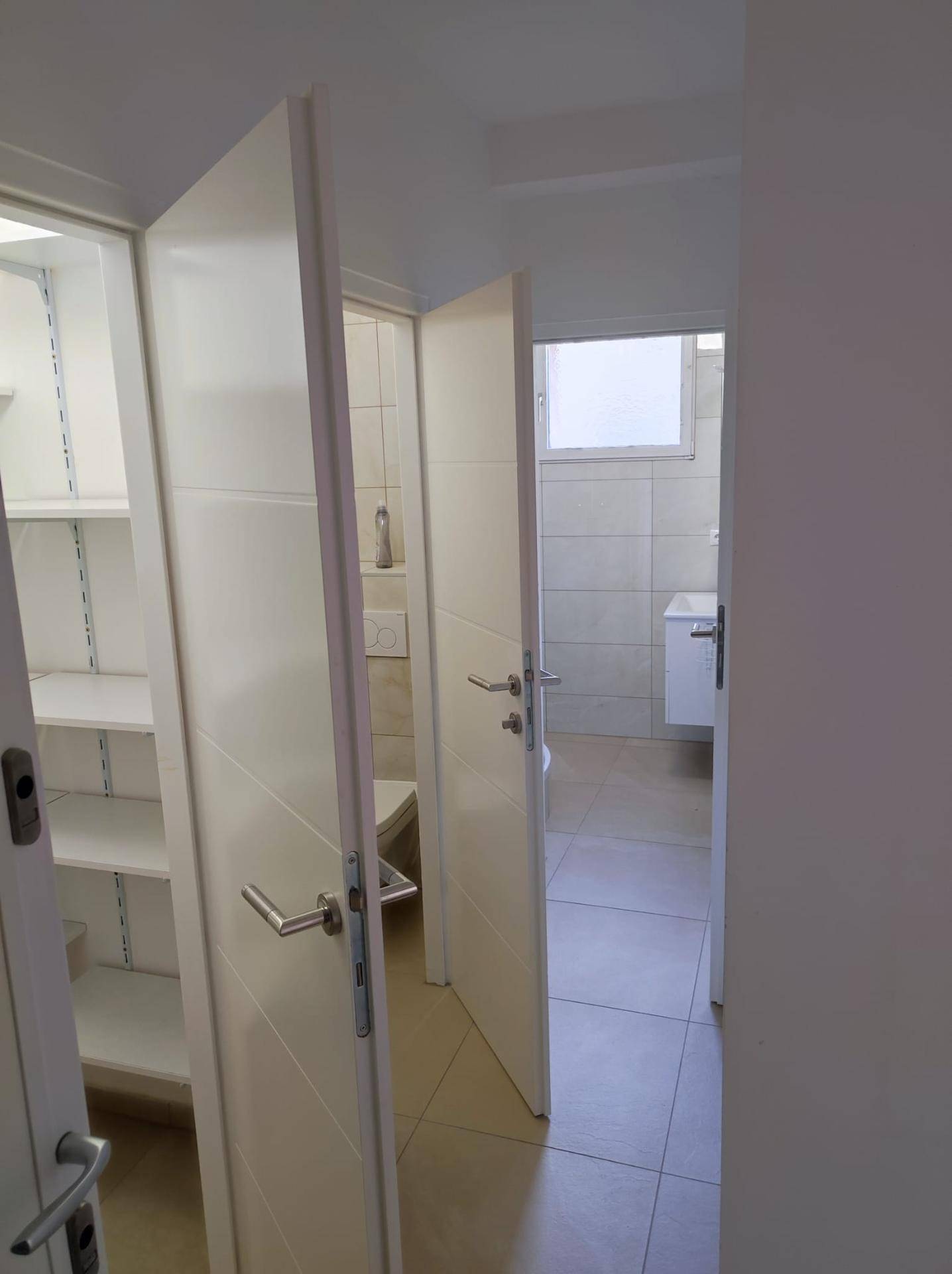 Heller Flur mit Zugang zu einem Badezimmer und einem praktischen Abstellraum mit Regalen.