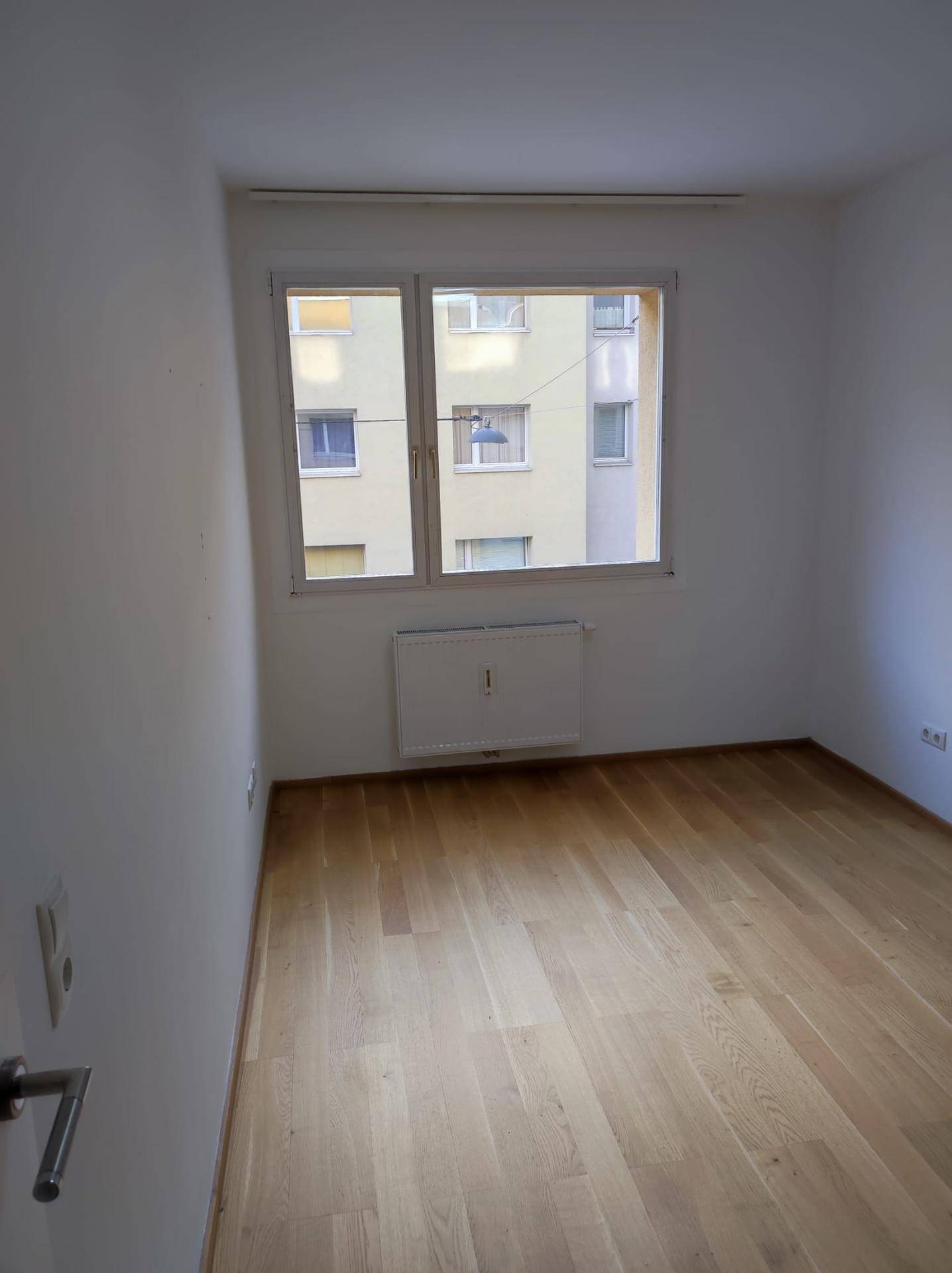 Heller Raum mit Parkettboden und einem Fenster, das den Blick auf die Umgebung bietet.