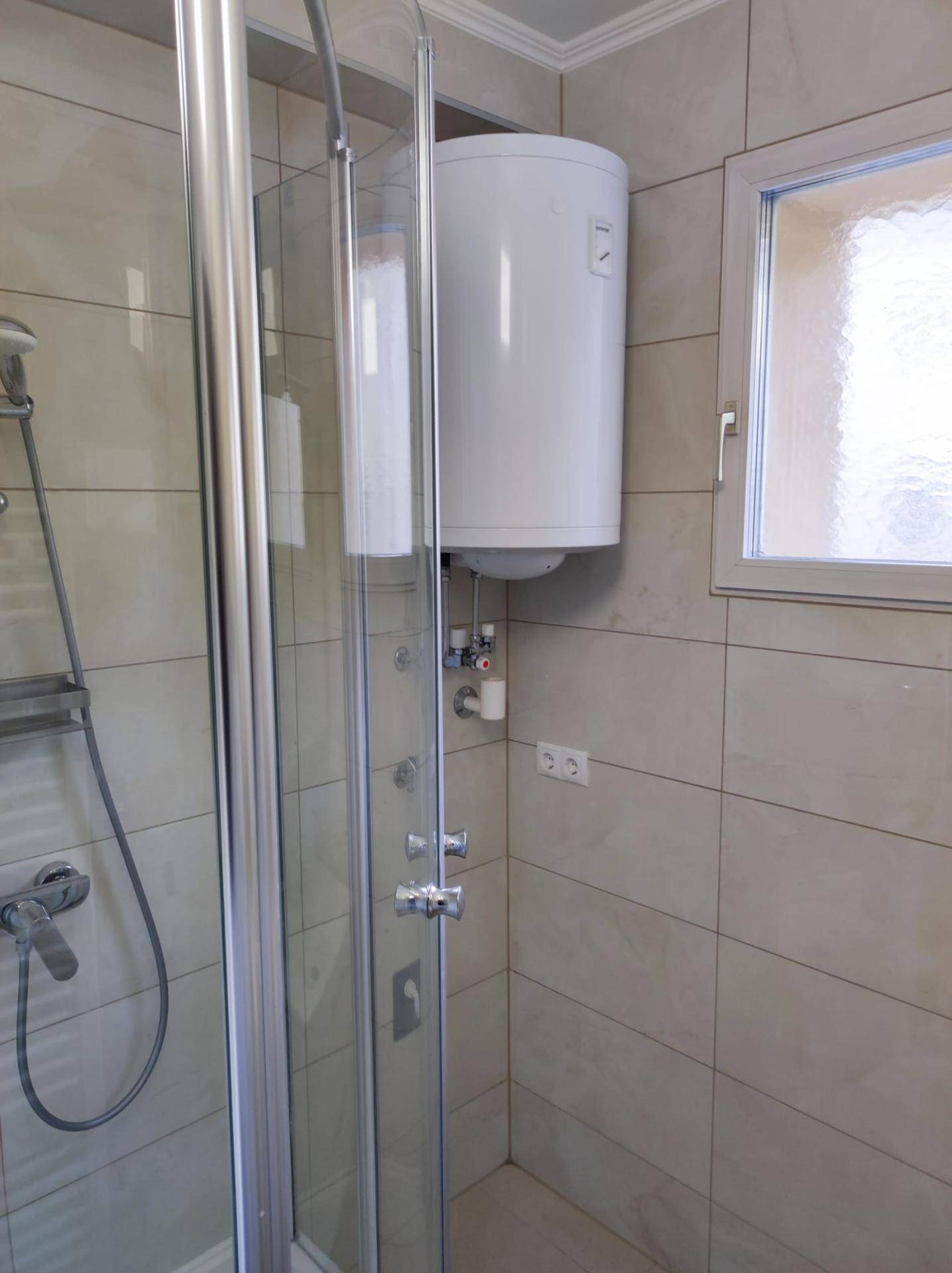 Badezimmer mit Duschkabine und einem an der Wand montierten Warmwasserboiler.